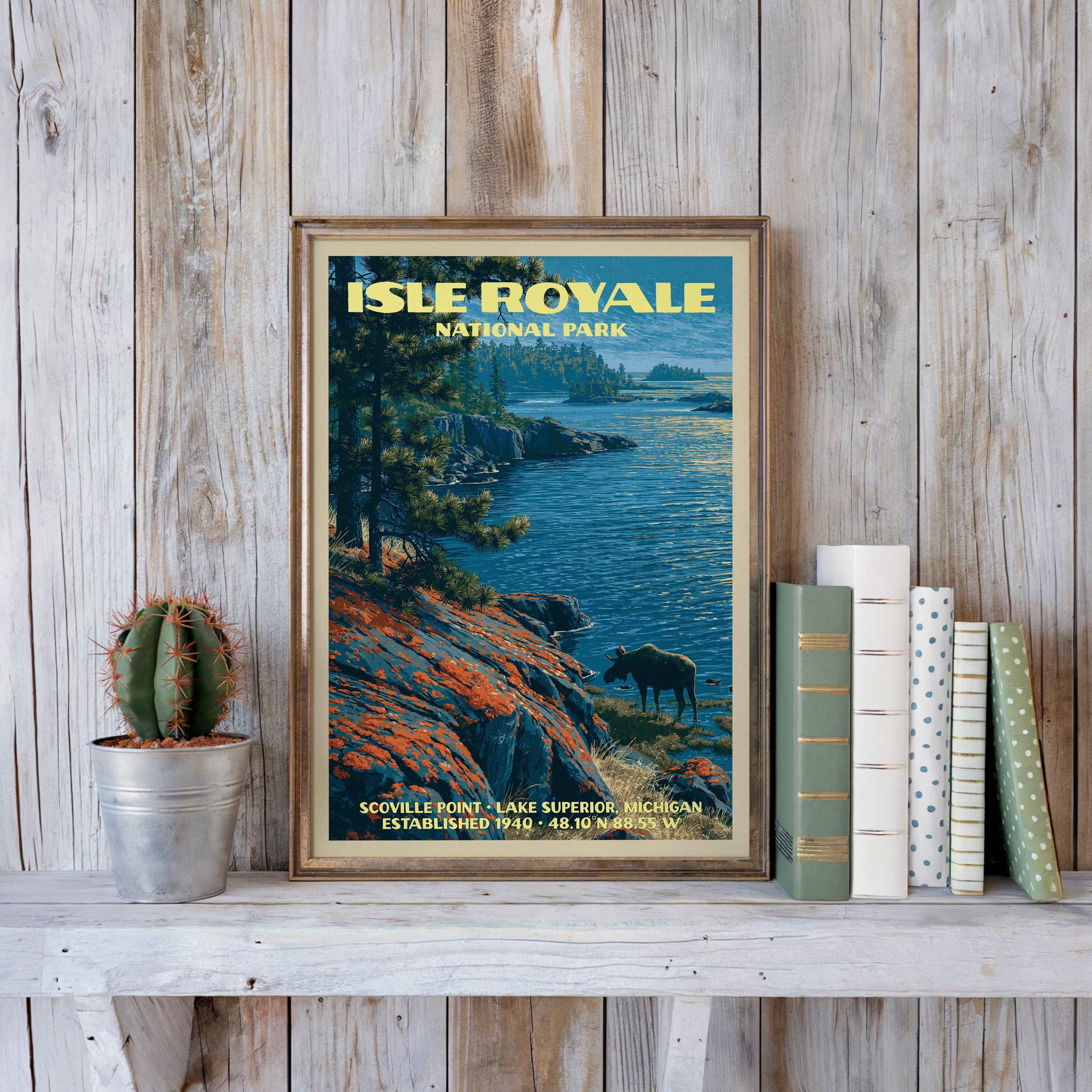 Isle Royale vintage poster in a slim gold frame on a whitewashed plank wall beside a cactus and pastel books