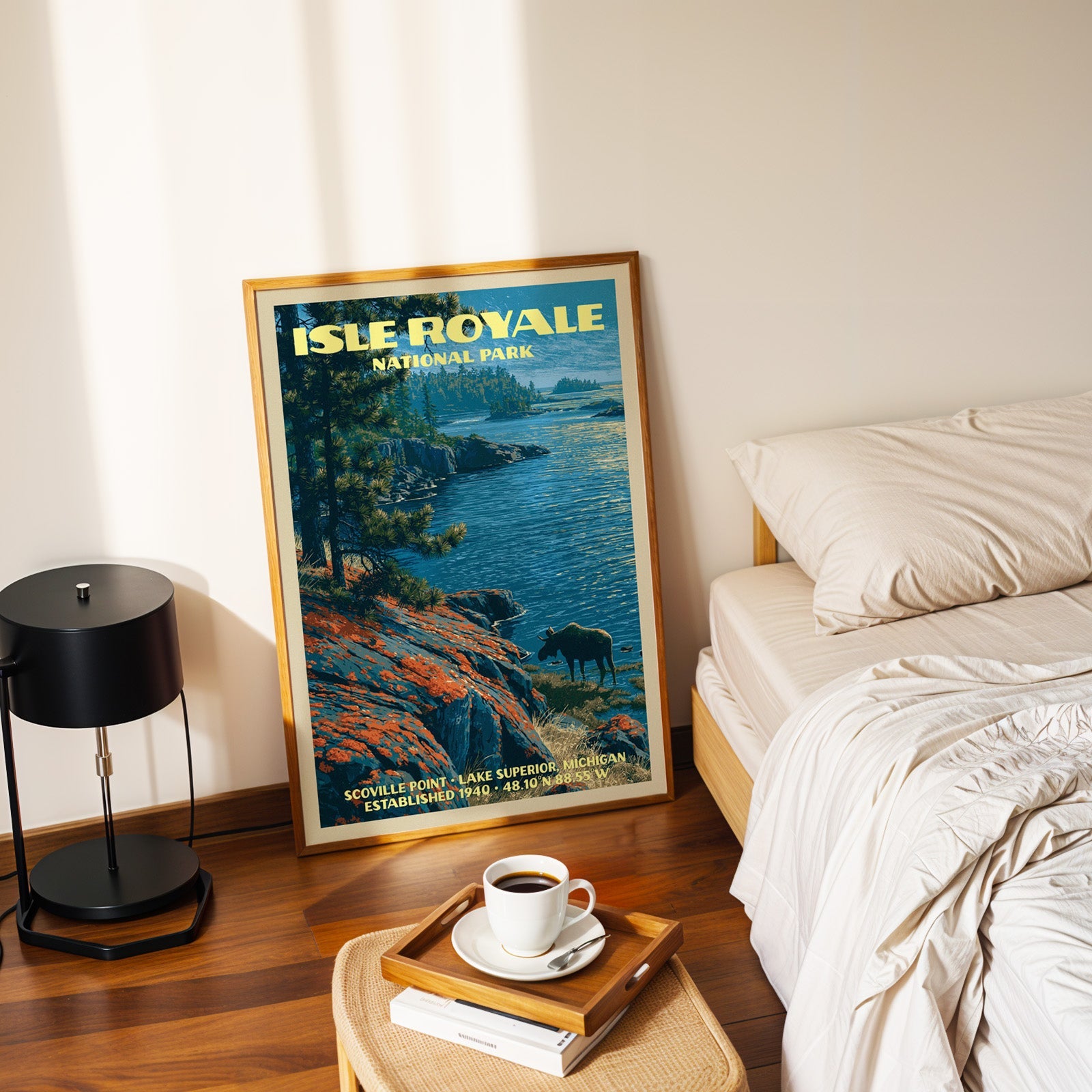 Isle Royale Scoville Point poster in a gold frame on the floor beside a made bed and a black table lamp