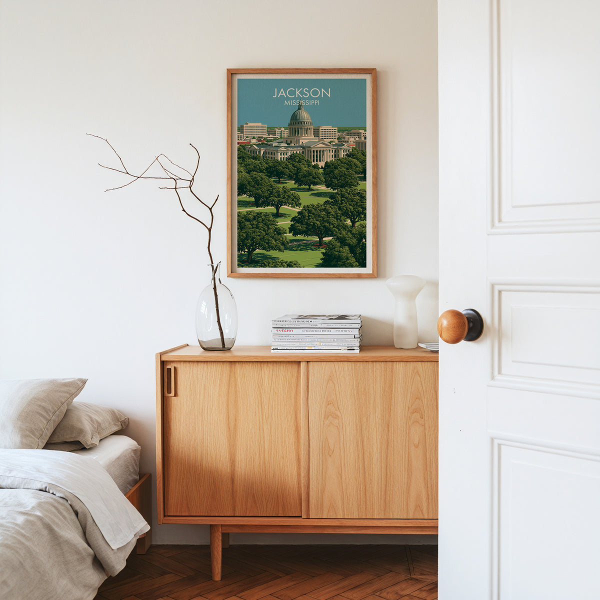 Jackson Mississippi poster in an oak frame on a light oak sideboard with dried stems, magazines and a vase.