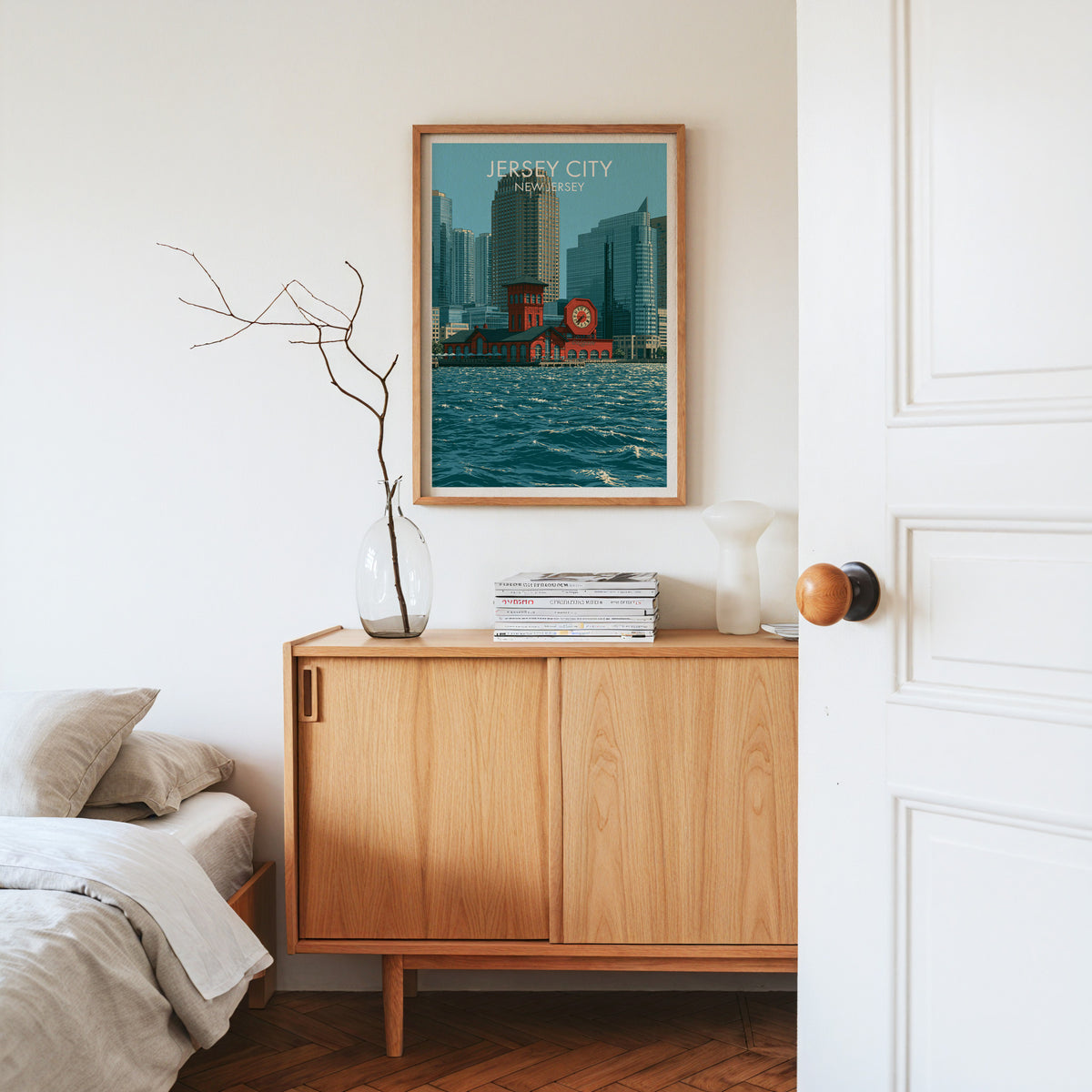 Jersey City poster in an oak frame on a light oak sideboard with dried stems, magazines and a white vase.