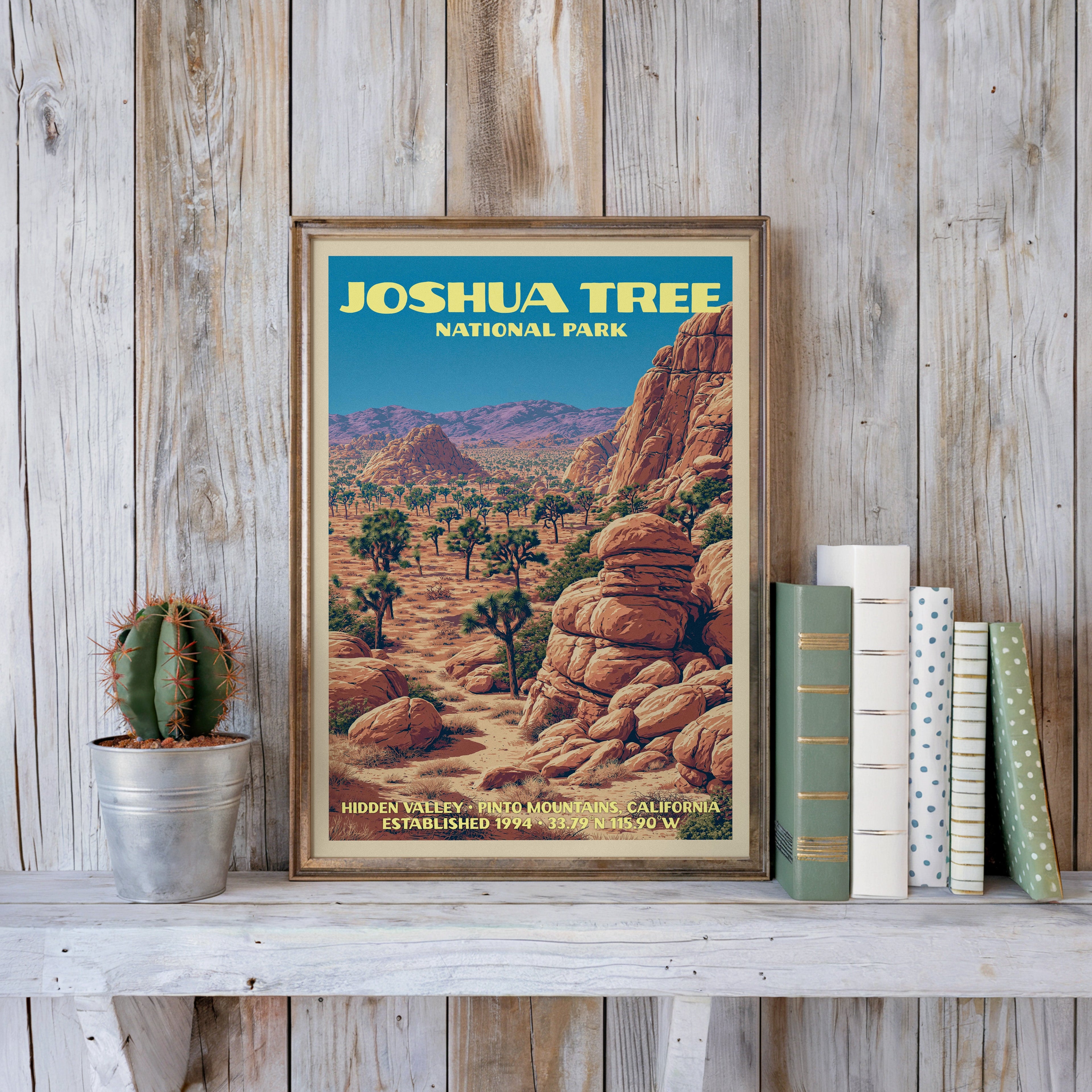 Joshua Tree vintage poster in a slim gold frame on a whitewashed plank wall beside a cactus and pastel books