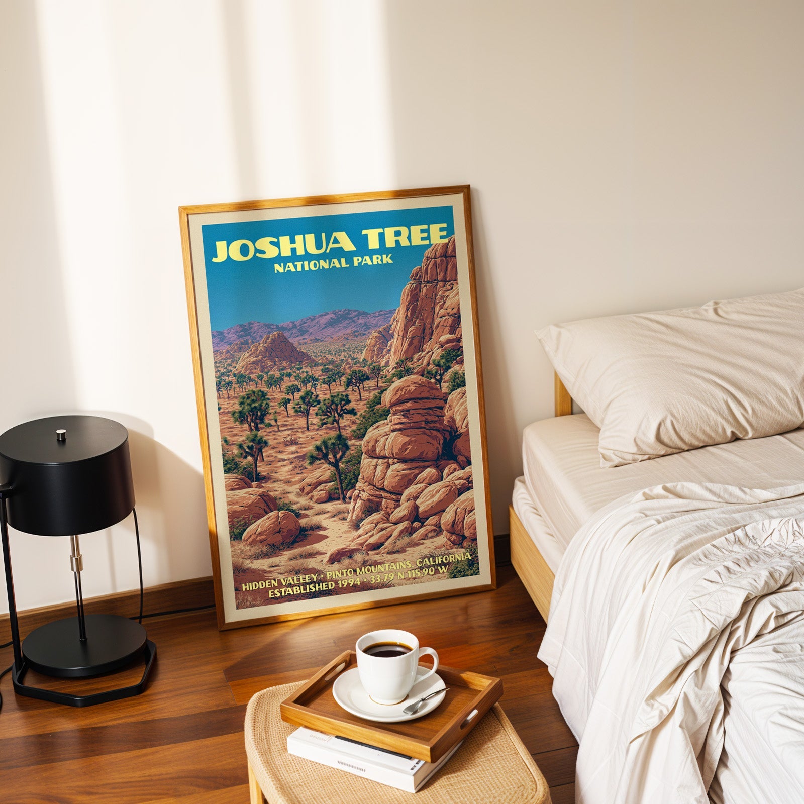 Joshua Tree Hidden Valley poster in a gold frame on the floor beside a made bed and a black table lamp