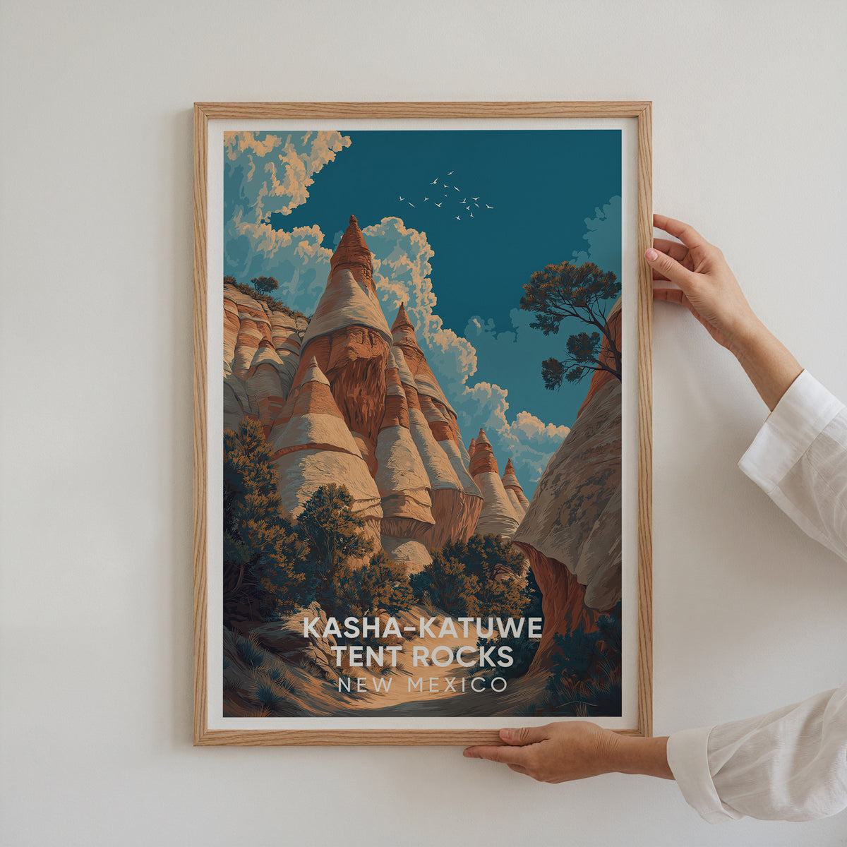 Two hands hold the oak-framed Tent Rocks travel poster up against a plain white wall.