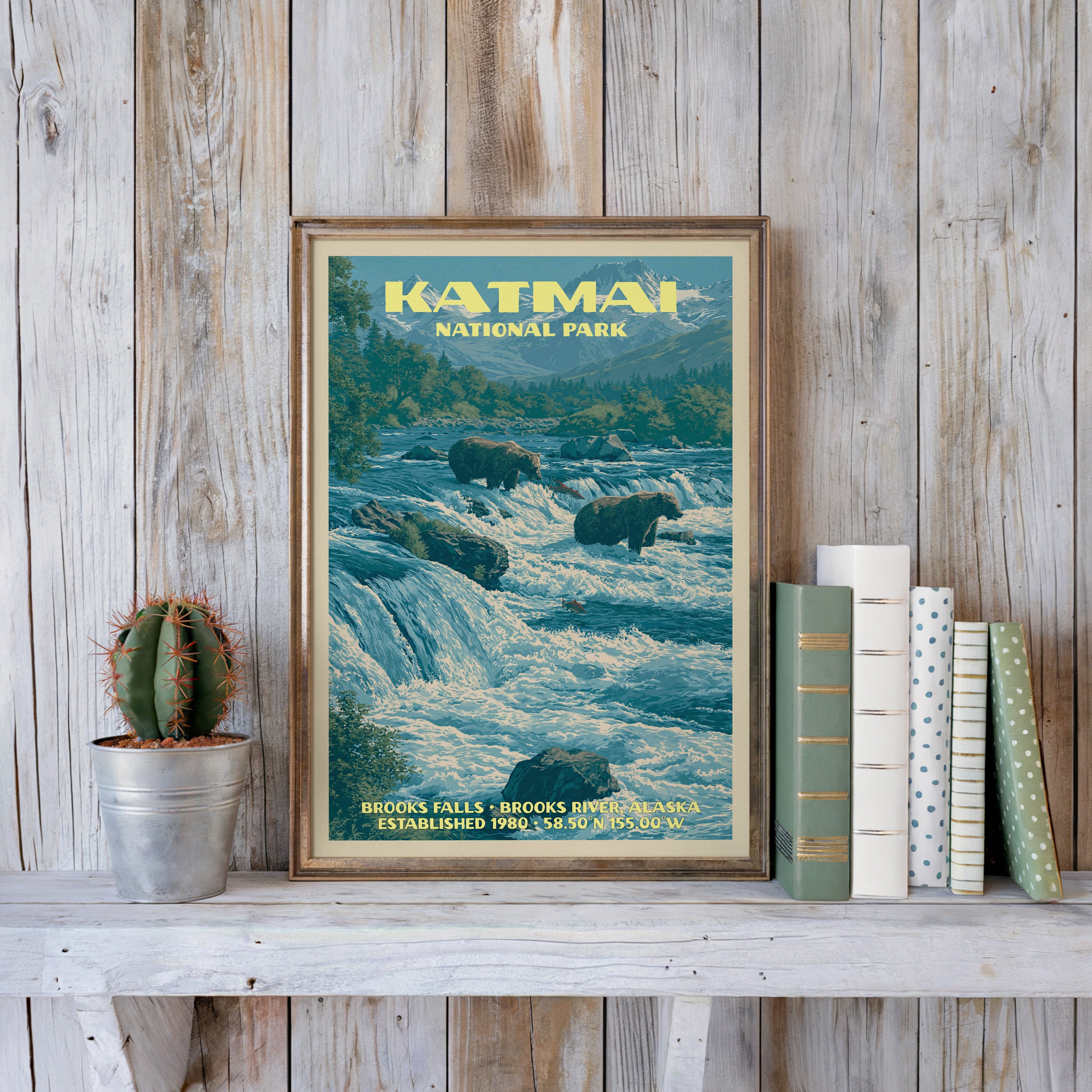Katmai vintage poster in a slim gold frame on a whitewashed plank wall beside a cactus and pastel books