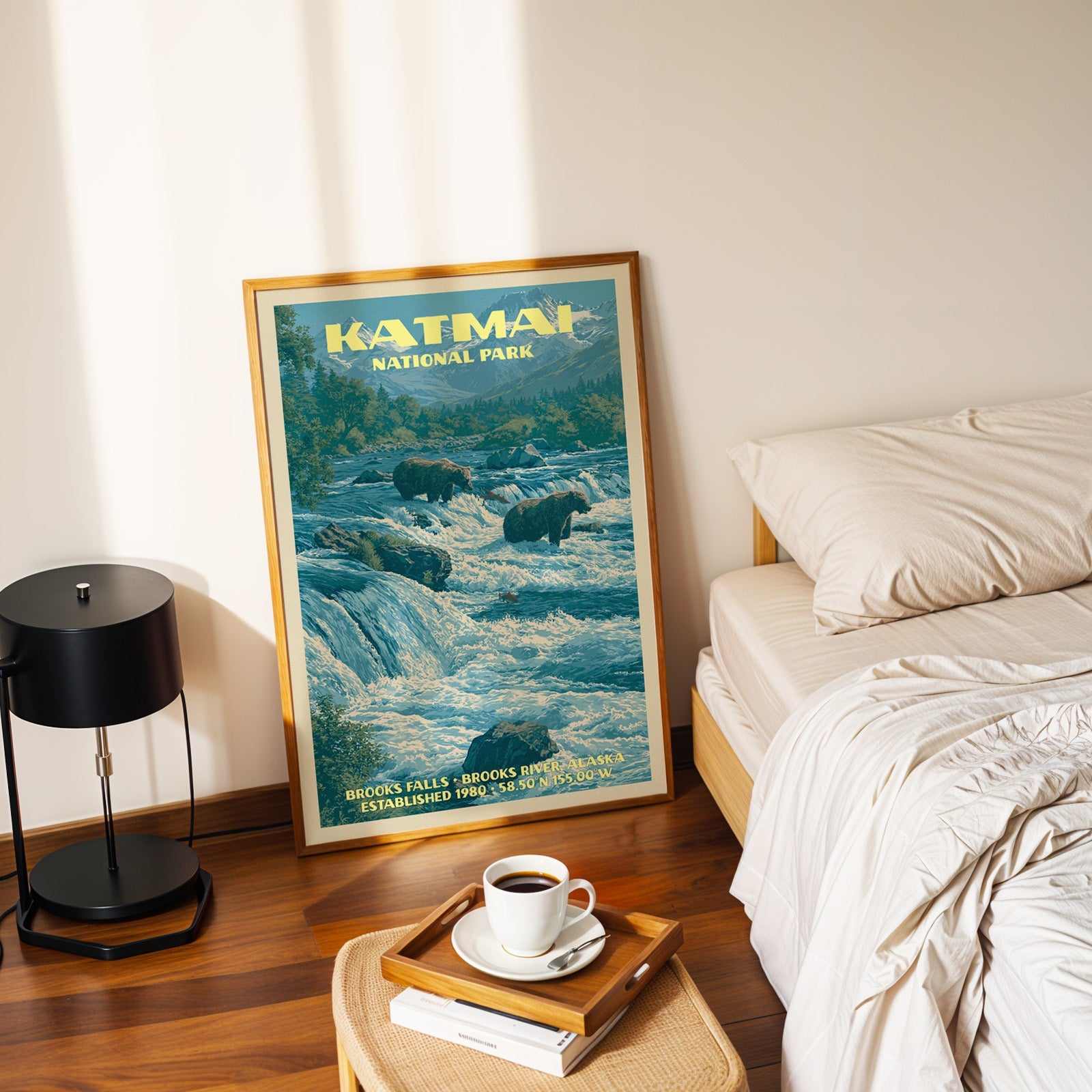 Katmai Brooks Falls poster in a gold frame on the floor beside a made bed and a black table lamp