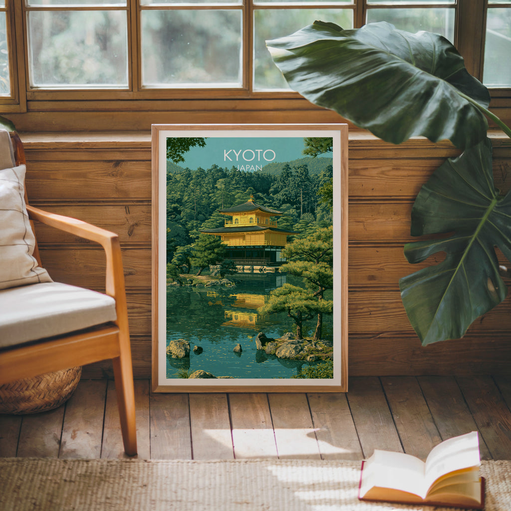 Framed Kinkakuji Golden Pavilion Kyoto poster leaning against a timber cabin wall with monstera leaves and an open book