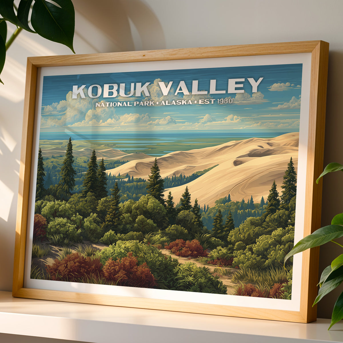 Kobuk Valley National Park wall art print in a light oak frame, leaning on a white shelf in warm sunlight beside a monstera plant
