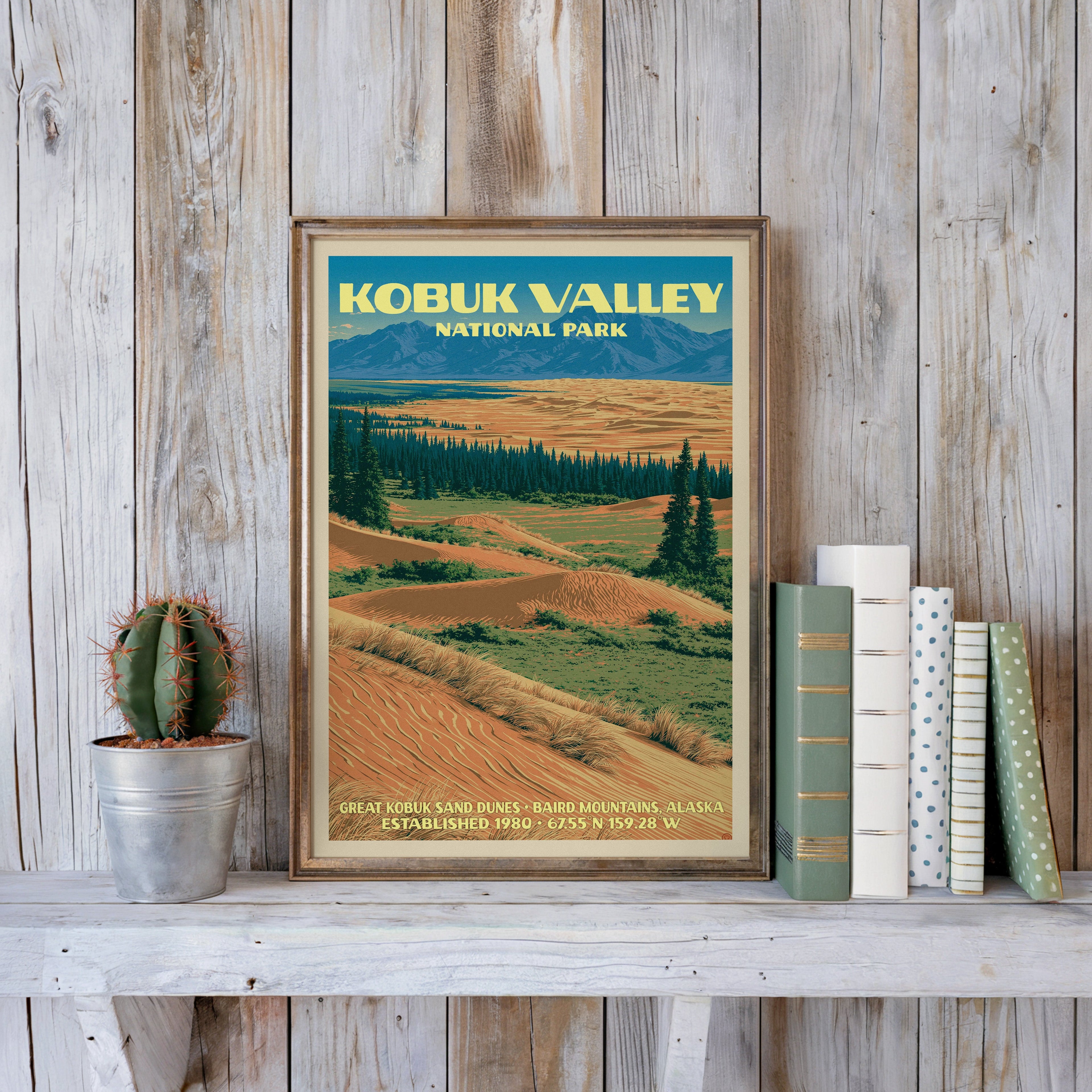 Kobuk Valley vintage poster in a slim gold frame on a whitewashed plank wall beside a cactus and pastel books