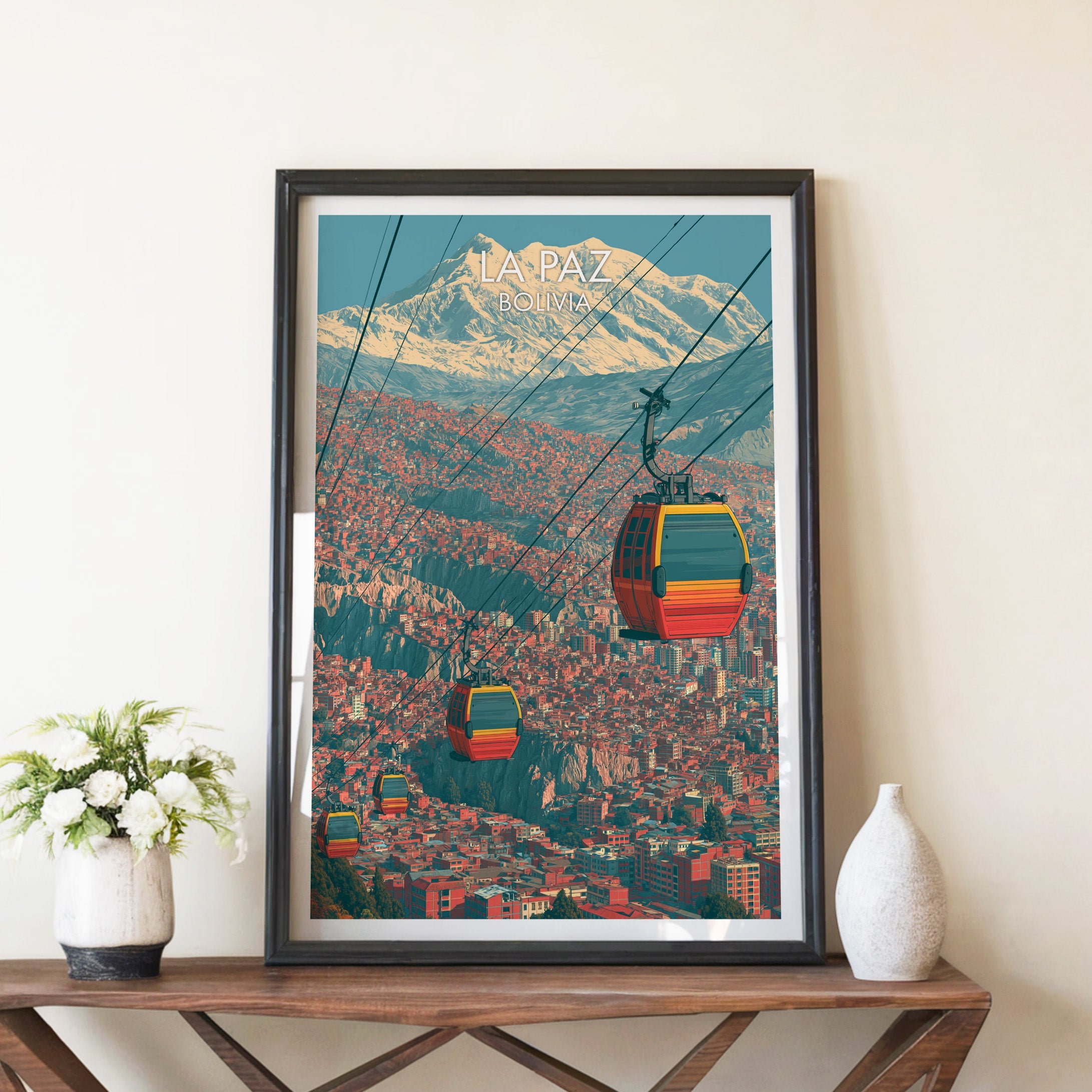La Paz gondola poster in a black frame on a brown X-leg console with white blooms and a pale ceramic vase