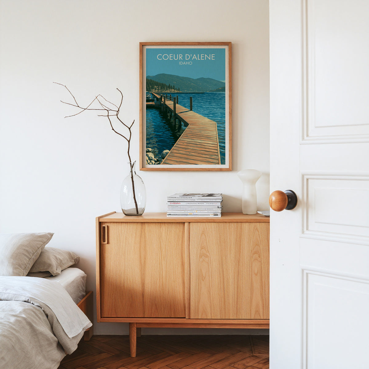 Lake pier poster in an oak frame on a light oak sideboard with dried stems, magazines and a white vase