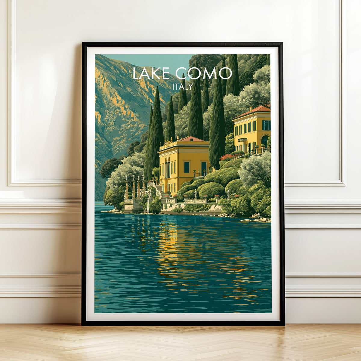 Lake Como villa print in a black frame leaning against a white panelled wall on a herringbone wood floor