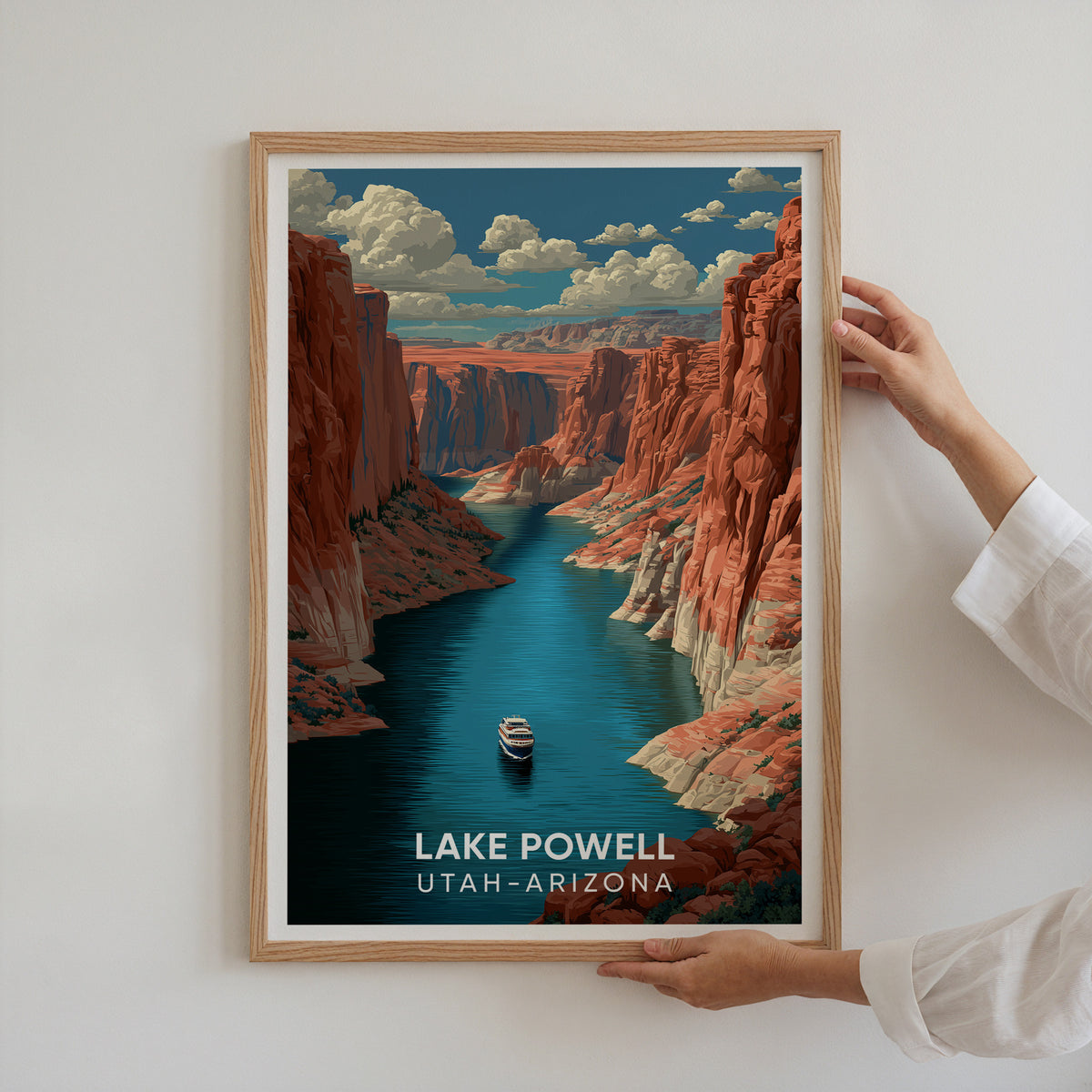 Two hands hold up the oak-framed Lake Powell travel poster against a plain white wall.