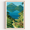 Lake Atitlan travel print in a light oak frame on a plain white wall, twin volcano cones above deep blue water