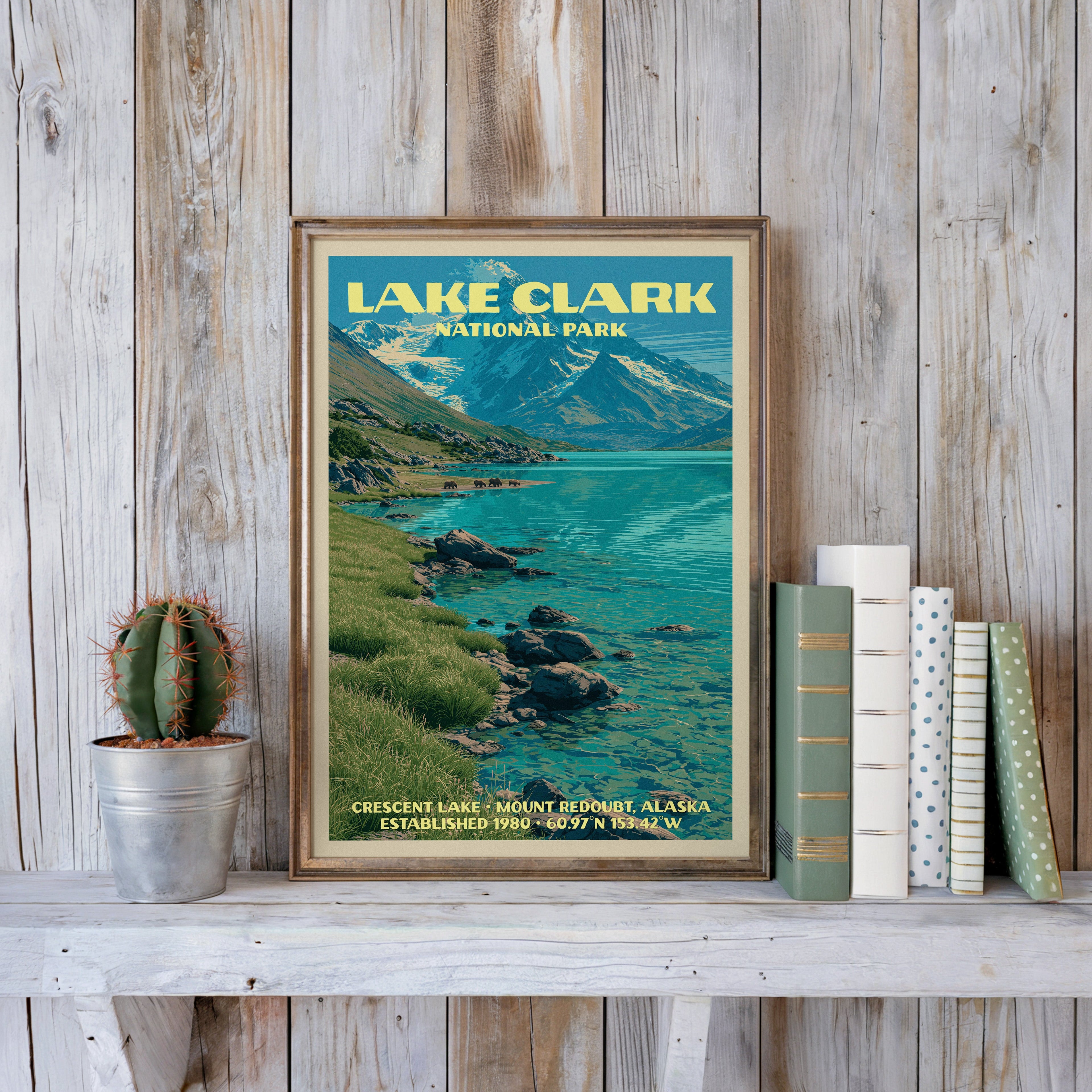 Lake Clark vintage poster in a slim gold frame on a whitewashed plank wall beside a cactus and pastel books