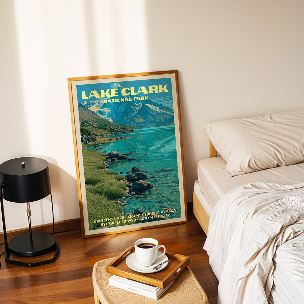 Lake Clark Crescent Lake poster in a gold frame on the floor beside a made bed and a black table lamp