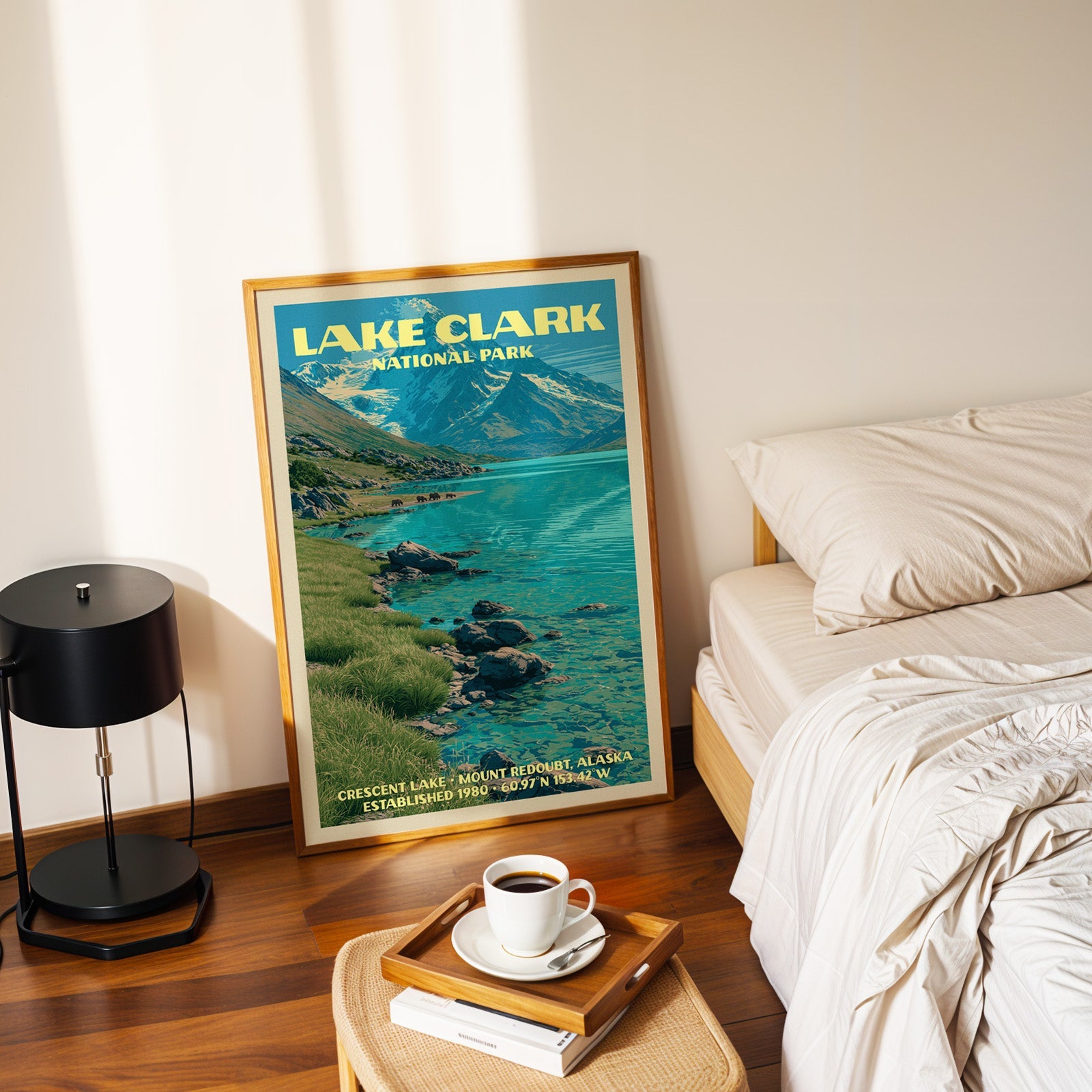 Lake Clark Crescent Lake poster in a gold frame on the floor beside a made bed and a black table lamp