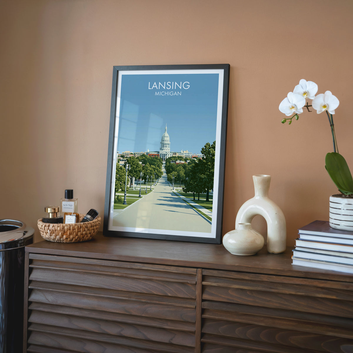 Lansing capitol wall art in a black frame on a walnut sideboard with a terracotta wall and rattan tray.