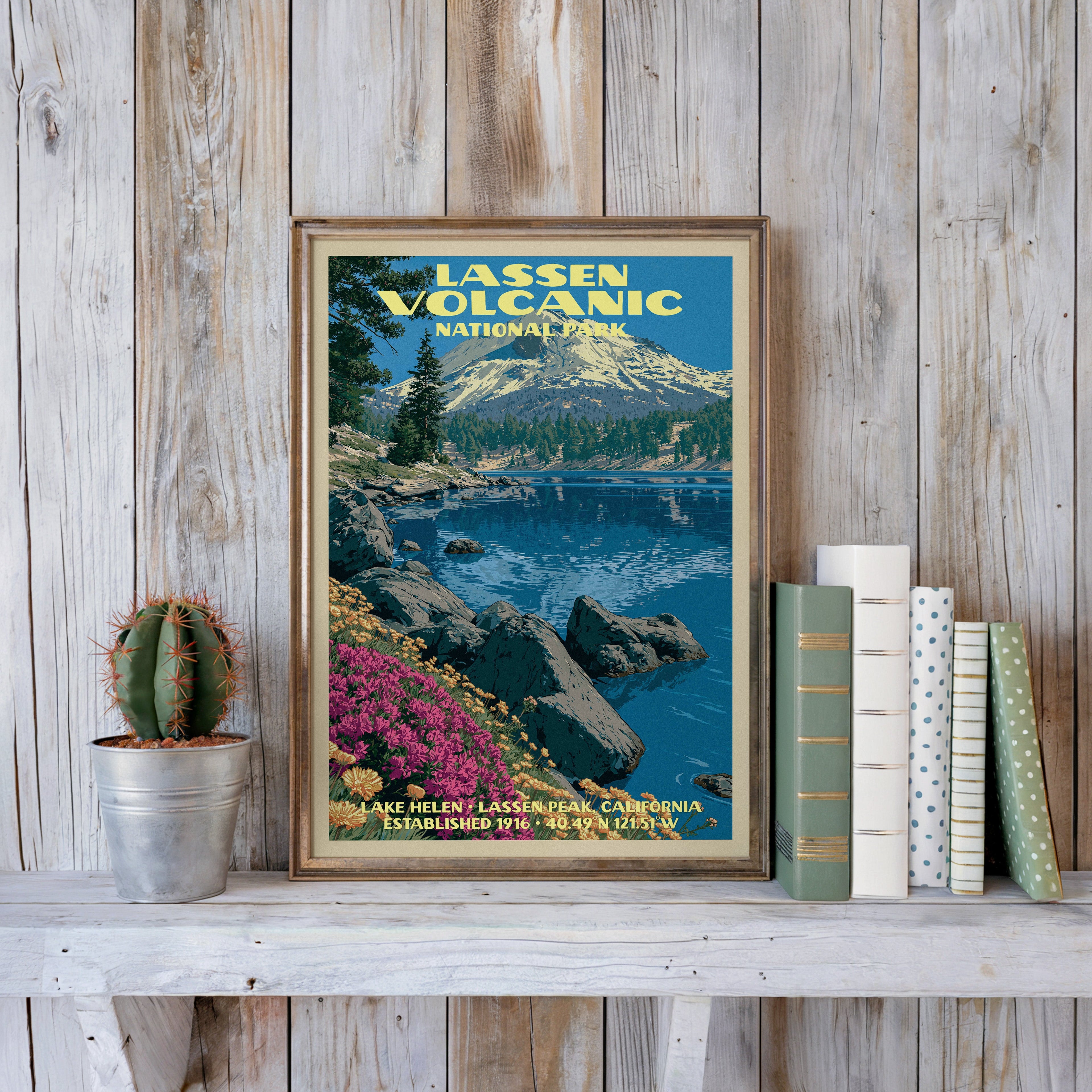 Lassen Volcanic vintage poster in a slim gold frame on a whitewashed plank wall beside a cactus and pastel books