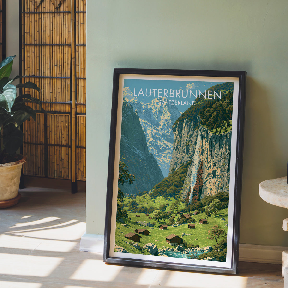 Lauterbrunnen poster, dark frame leaning on a sage-green wall beside a bamboo screen and a peace lily