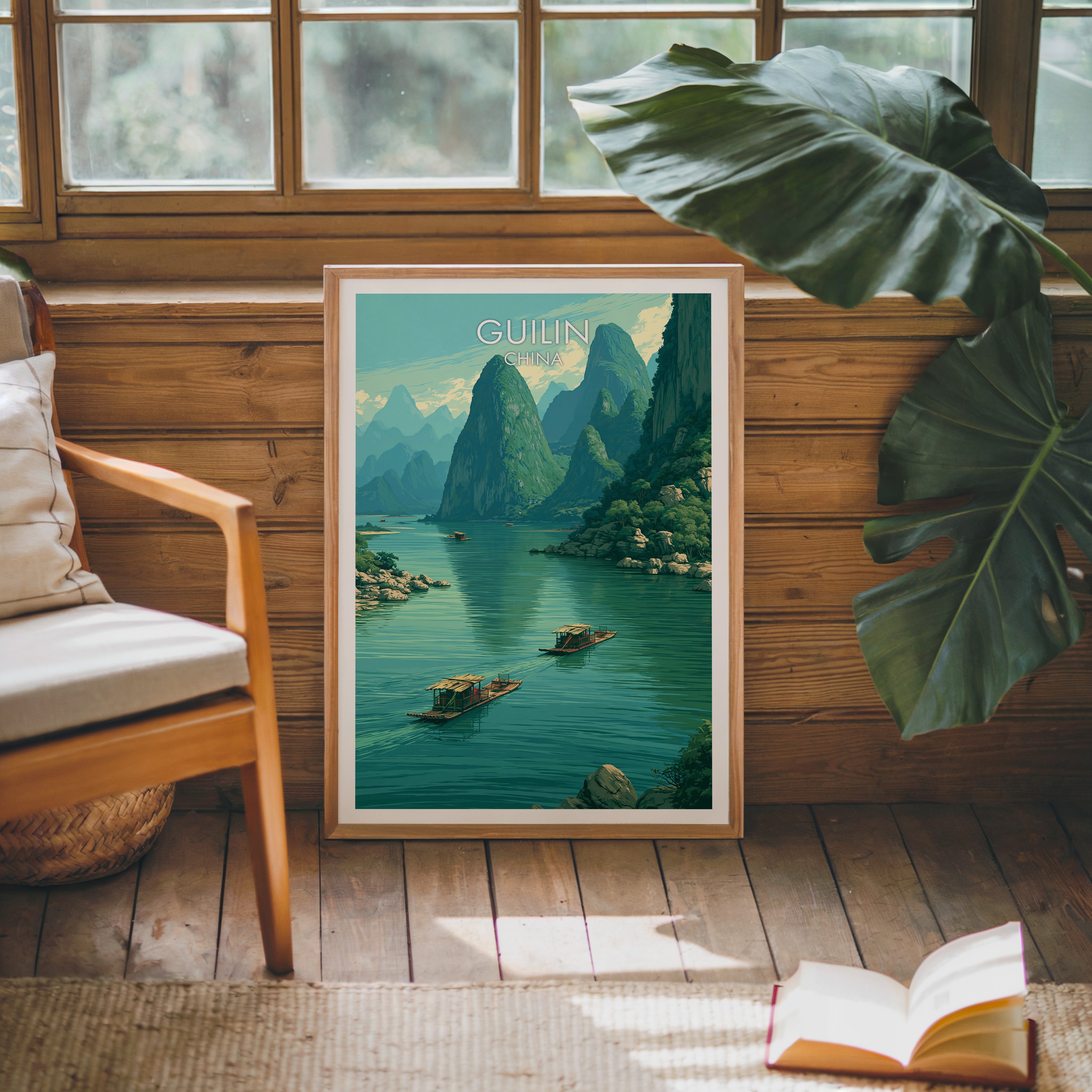 Framed Li River Guilin China poster leaning against a timber cabin wall with monstera leaves and an open book