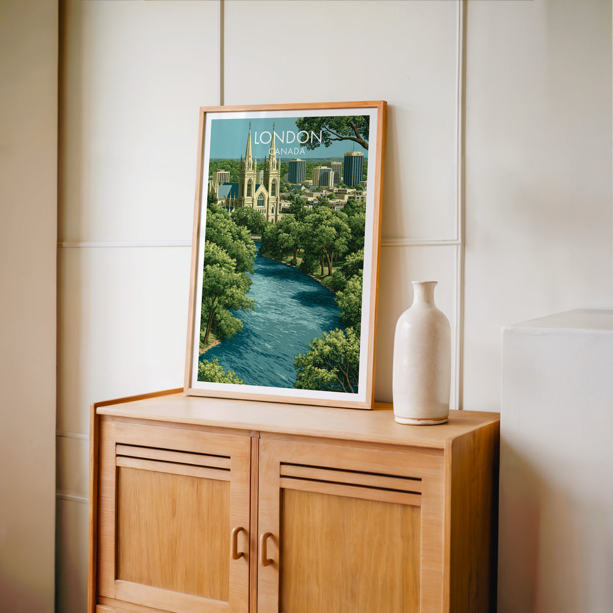 Forest City river canopy wall art in an oak frame on a light wood cabinet beside a stoneware vase
