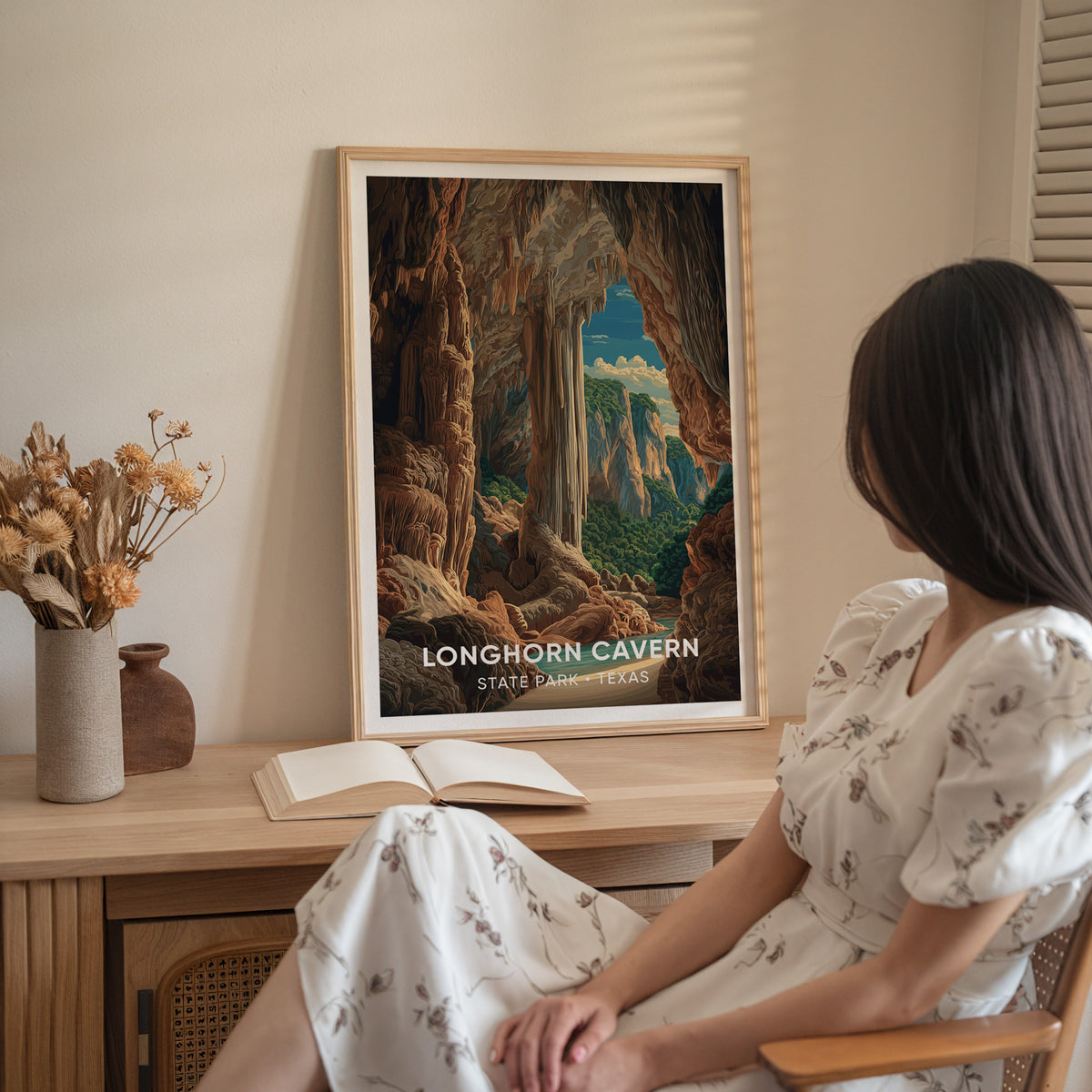 A woman in a white dress sits beside the oak-framed Longhorn Cavern print on a sideboard of dried flowers.