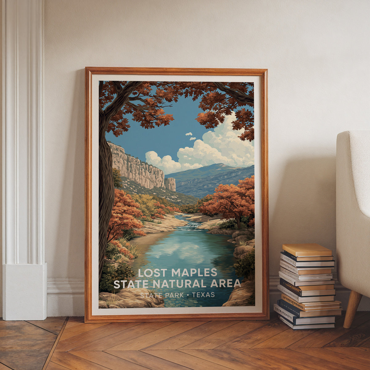 Lost Maples canvas print in a walnut frame on herringbone floors beside a book stack and cream chair