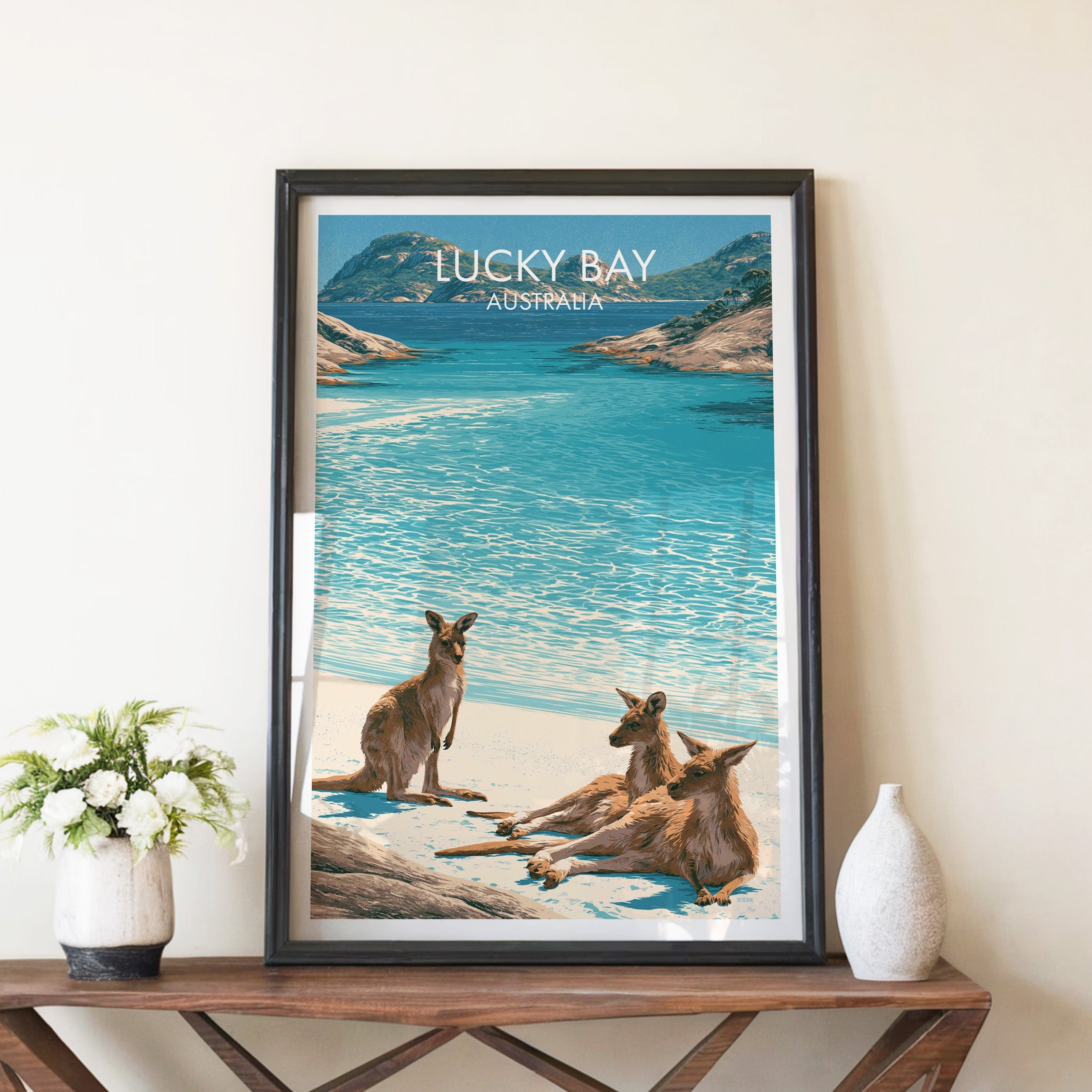 Kangaroos on the beach print in a black frame on a walnut console with white peonies and a stone vase