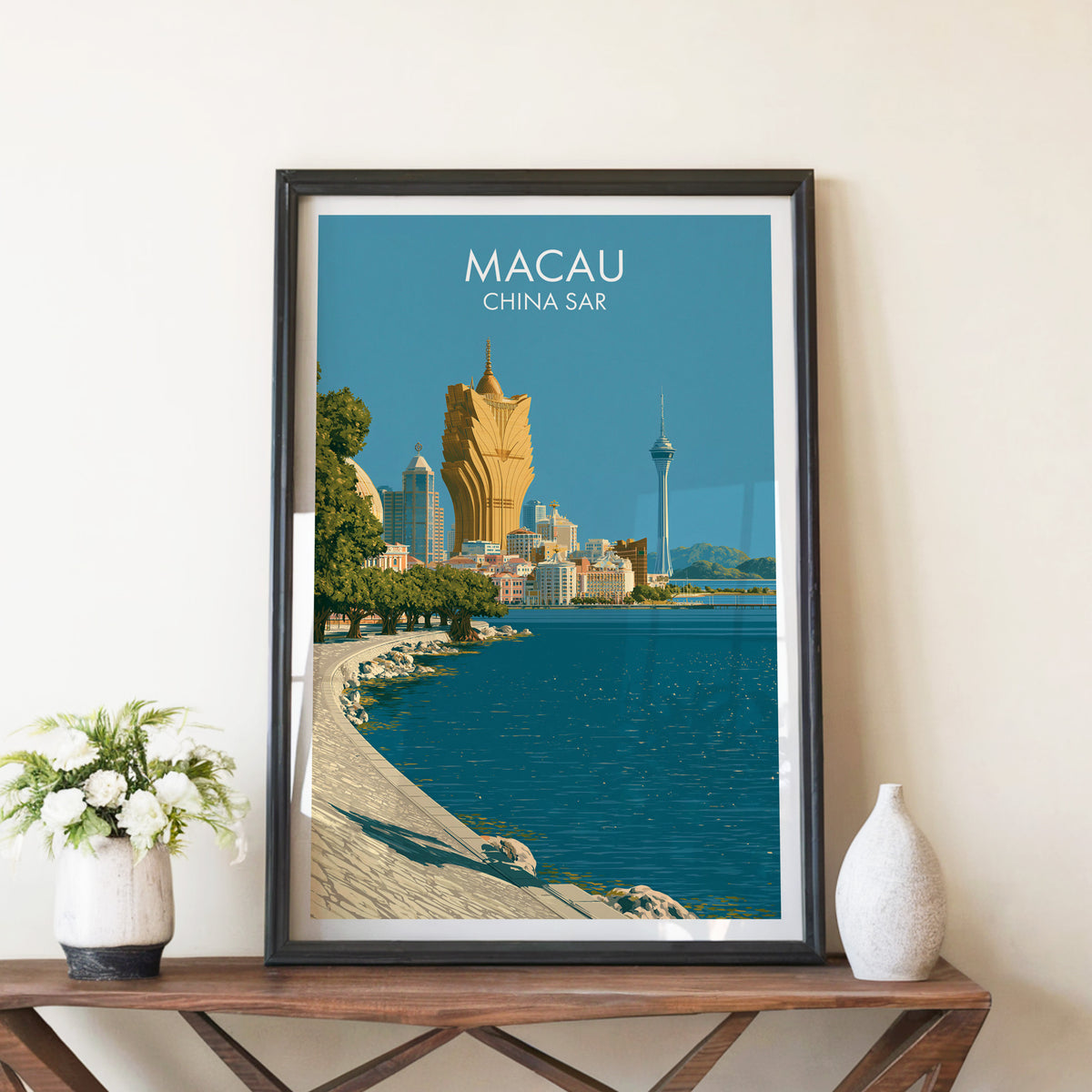 Macau lakeside promenade print in a black frame on a walnut console table beside white peonies in a stone vase