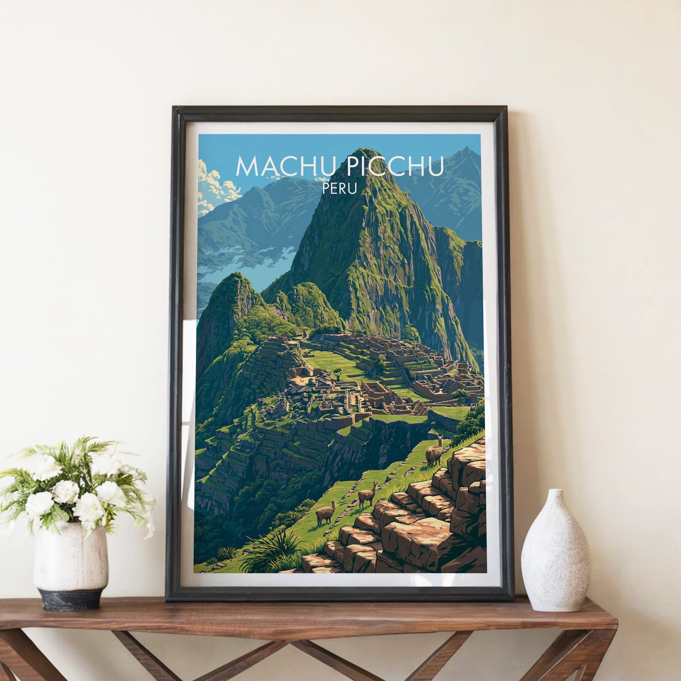 Inca citadel print in a black frame on a brown console table beside white flowers in a ceramic vase