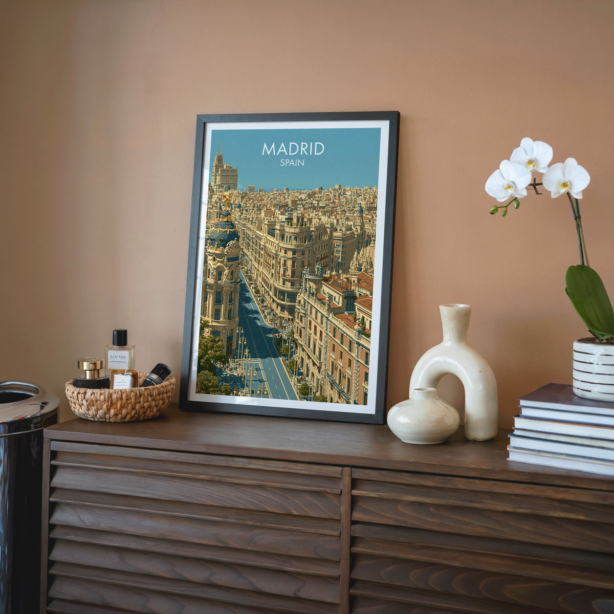 Gran Via Madrid wall art, black frame on a walnut sideboard against a terracotta wall with a white orchid