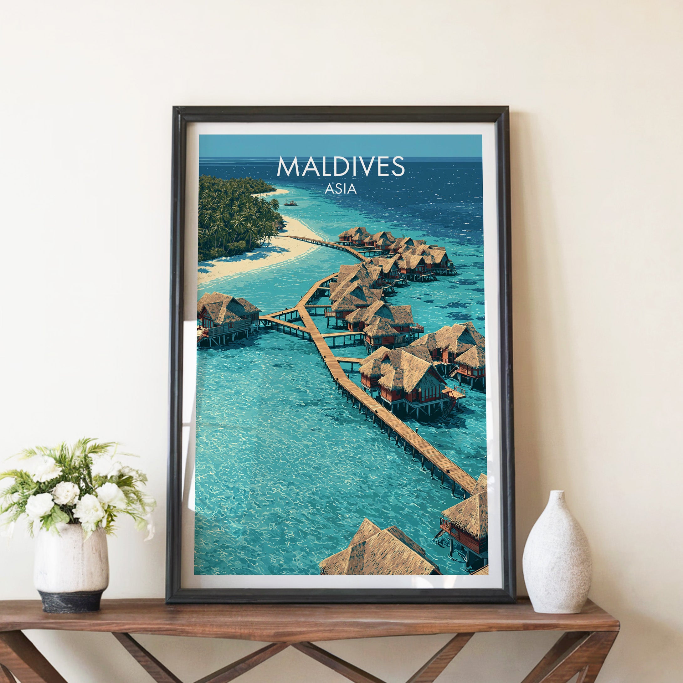 Maldives travel poster in a black frame on a wooden console table with white flowers
