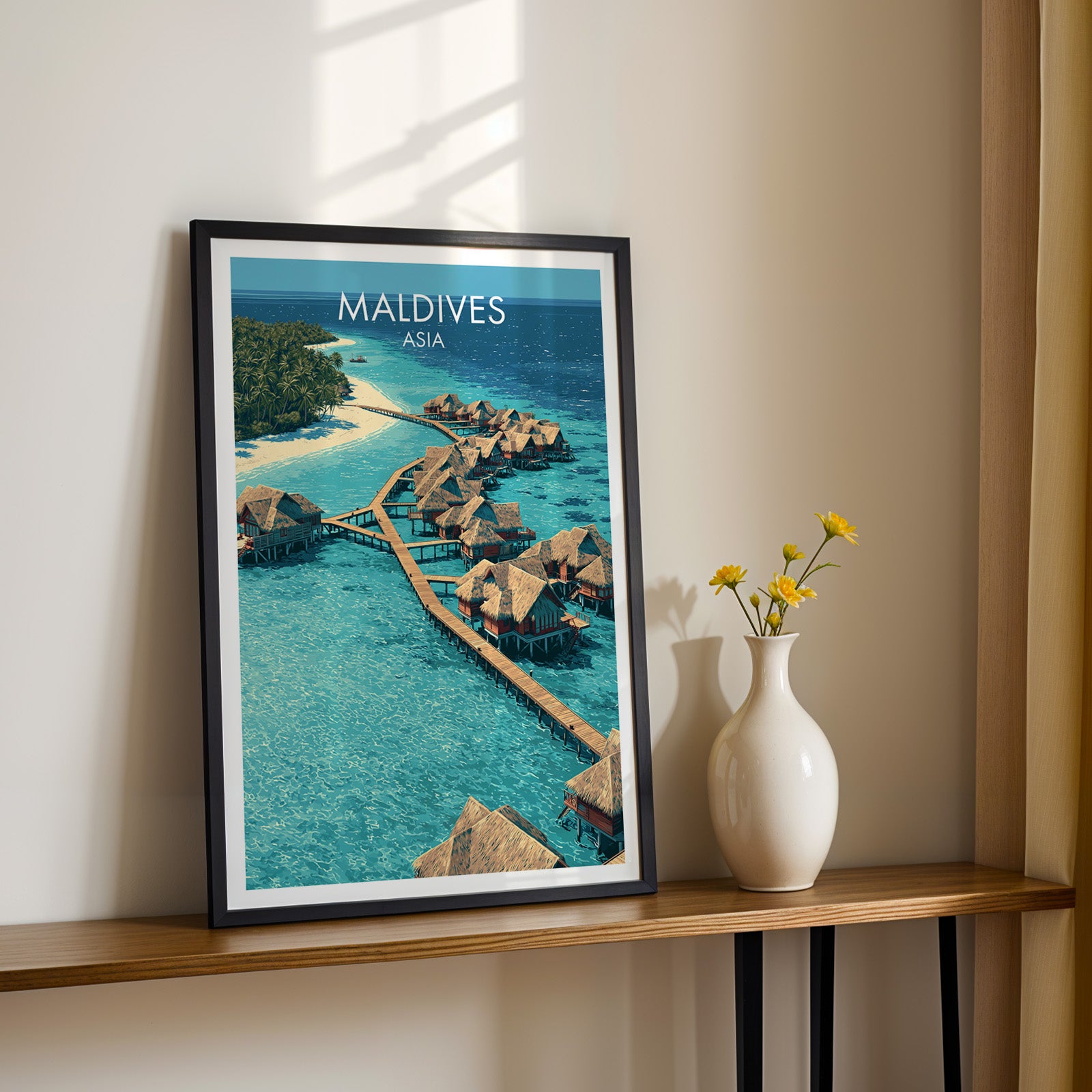 Black framed Maldives print on a narrow hallway console in sunlight, styled with yellow flowers