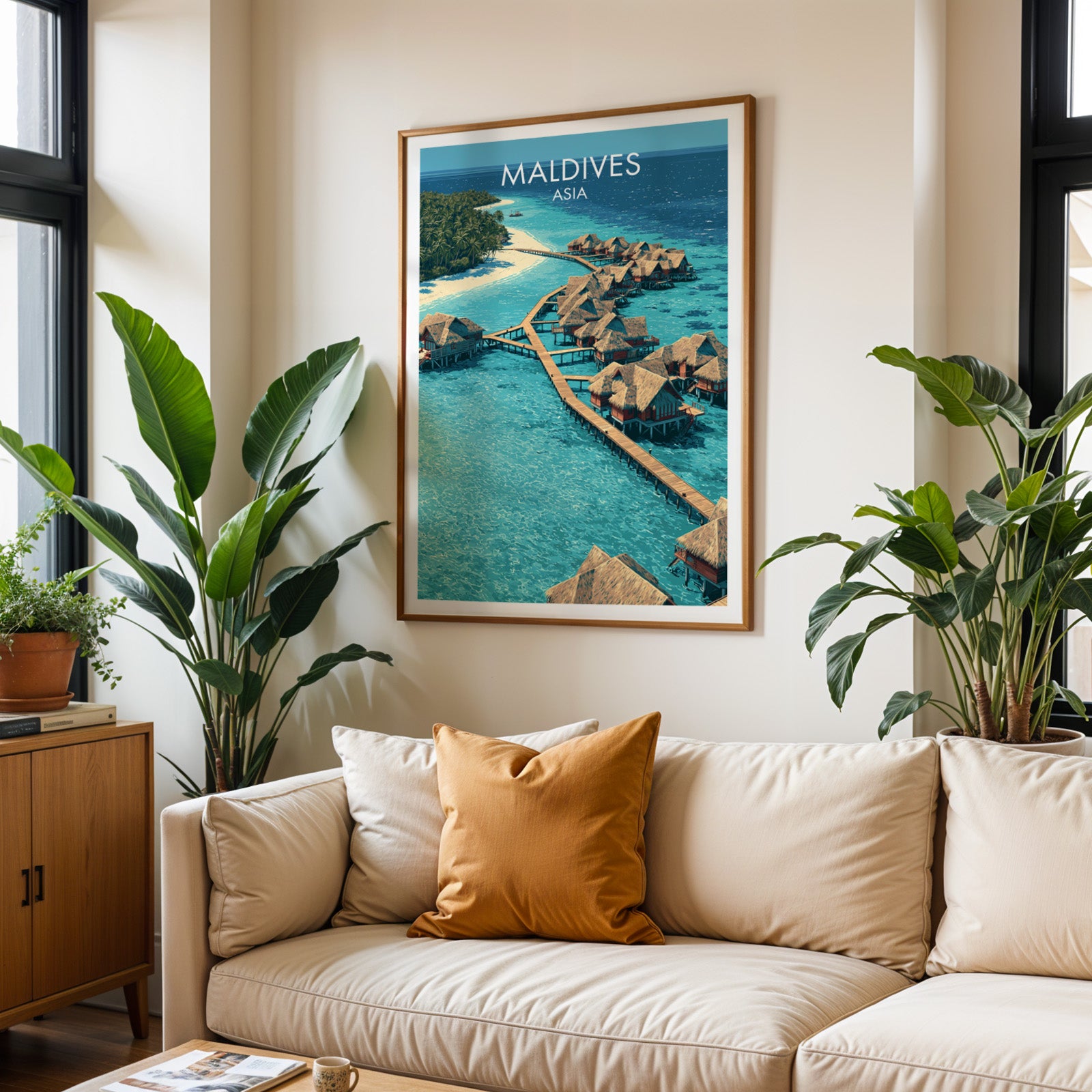 Framed Maldives wall art hanging above a cream sofa in a bright living room with tropical plants