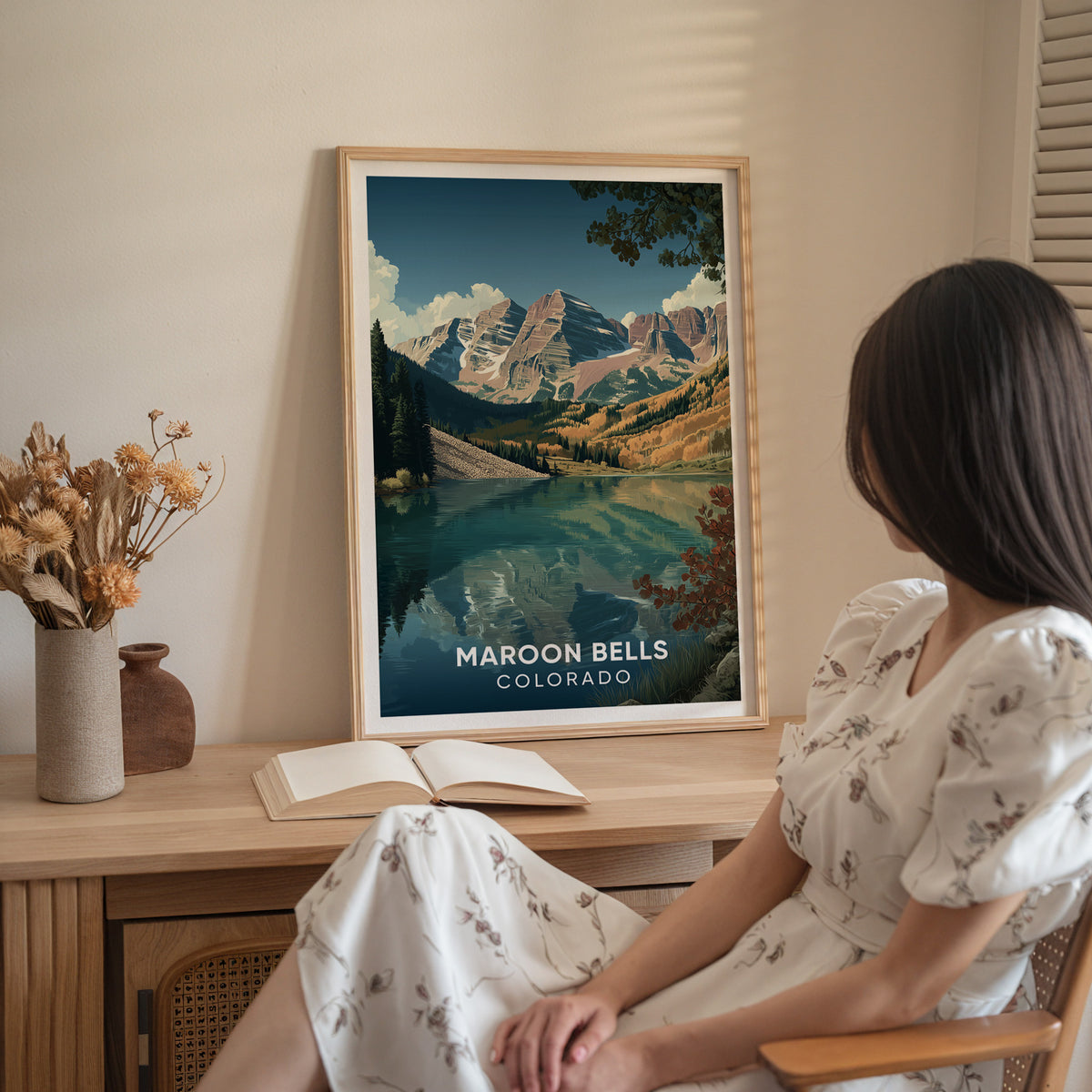 A seated woman in a white dress next to the oak-framed Maroon Bells print on a wood sideboard