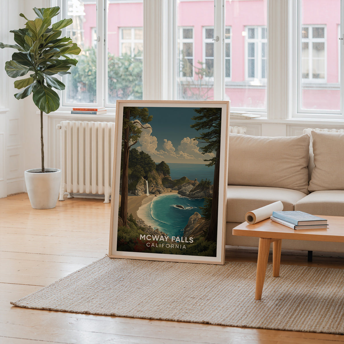 McWay Falls wall art leaning by a window with a pink facade outside and a cream sofa behind