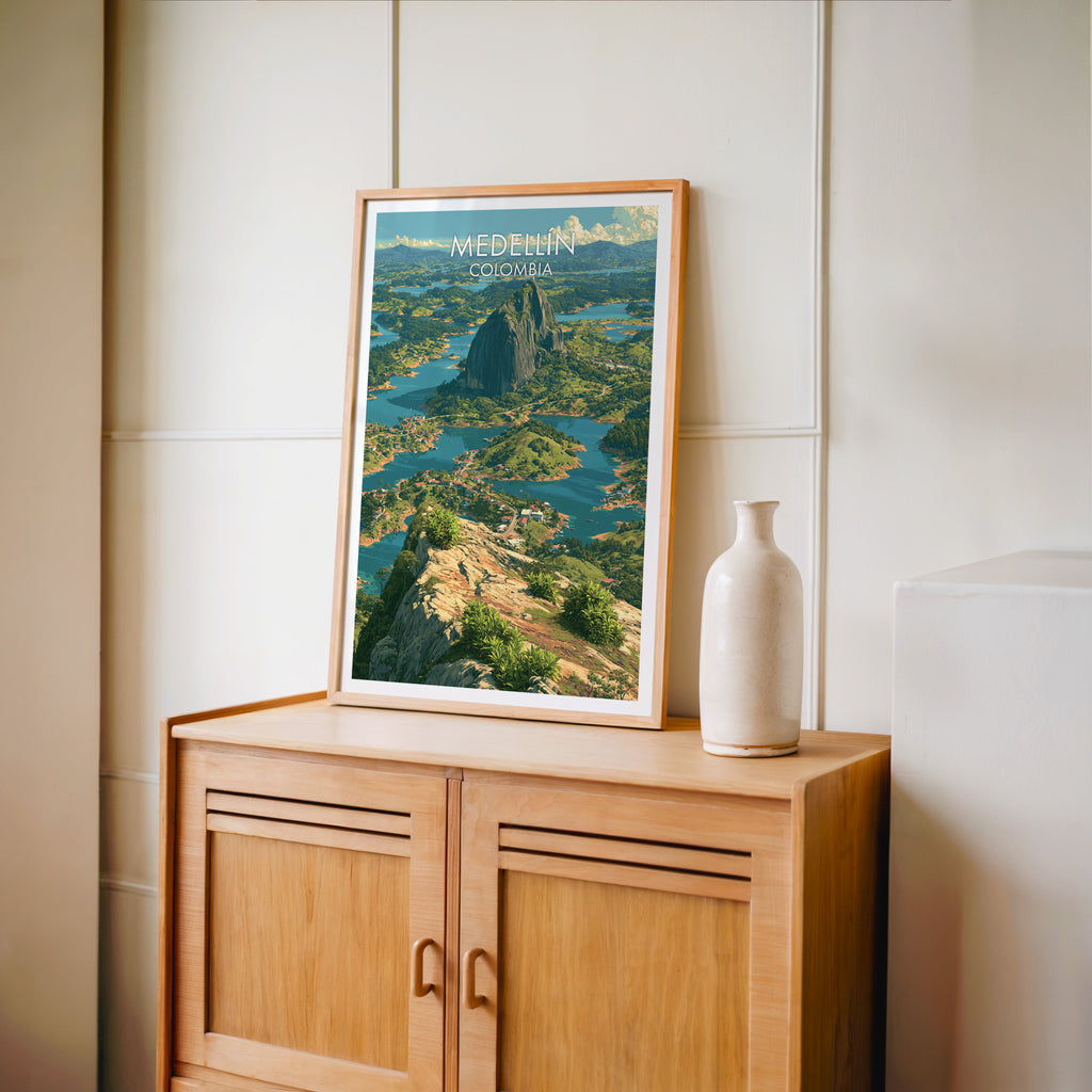 Medellin travel poster in an oak frame standing on a light oak cabinet against a cream panelled wall with a tall vase