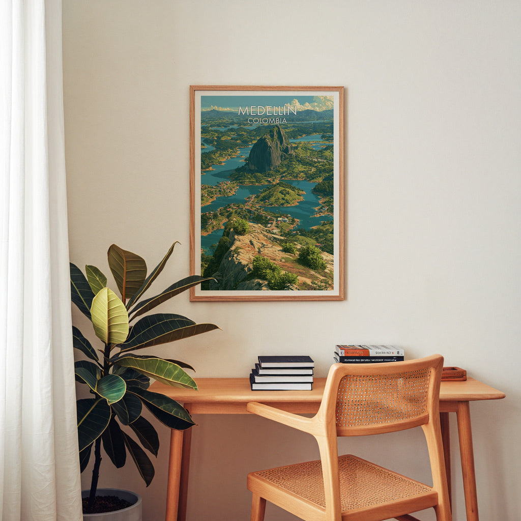 Medellin lake print in an oak frame above a wood desk with a cane chair, stacked books and a rubber plant, home office