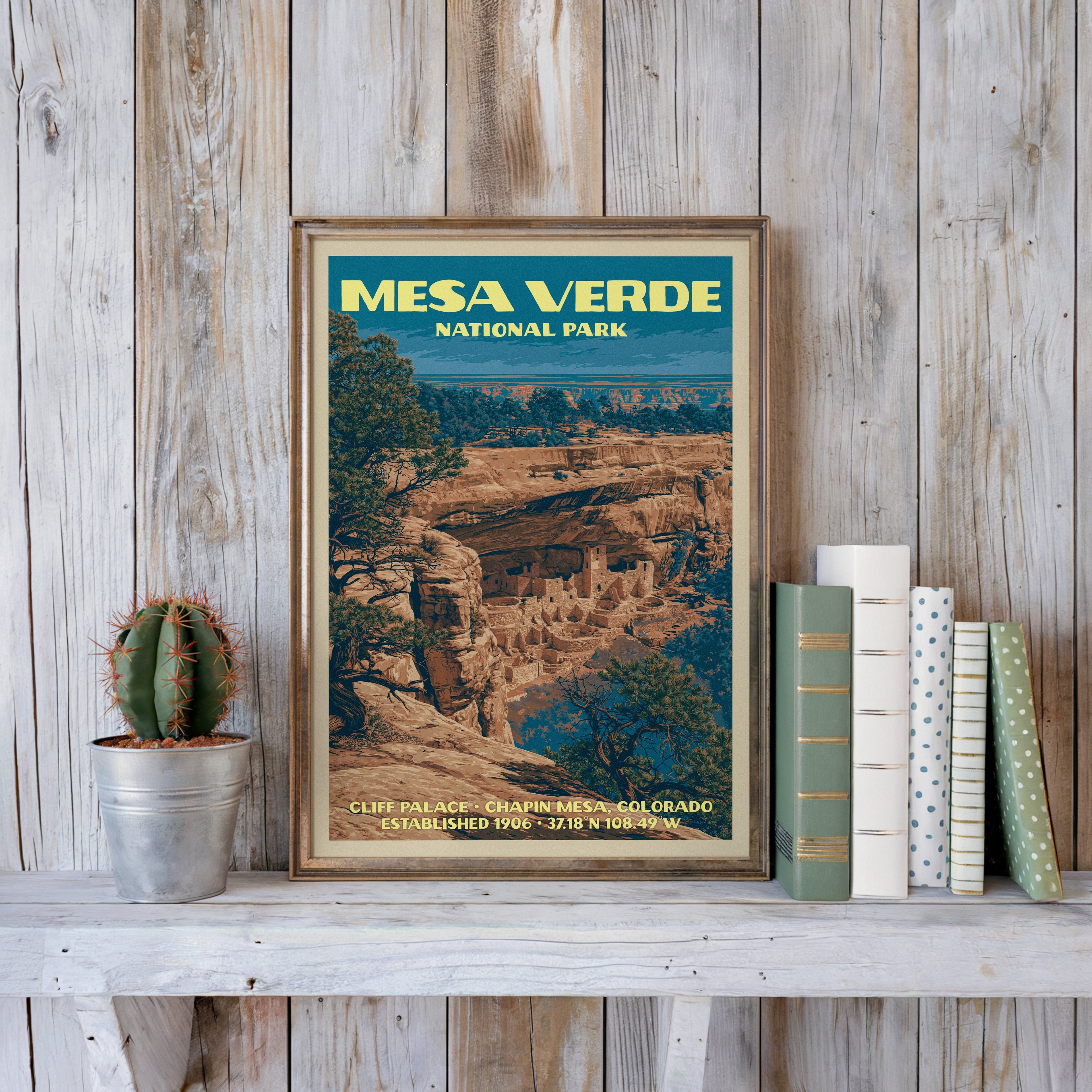 Mesa Verde vintage poster in a slim gold frame on a whitewashed plank wall beside a cactus and pastel books