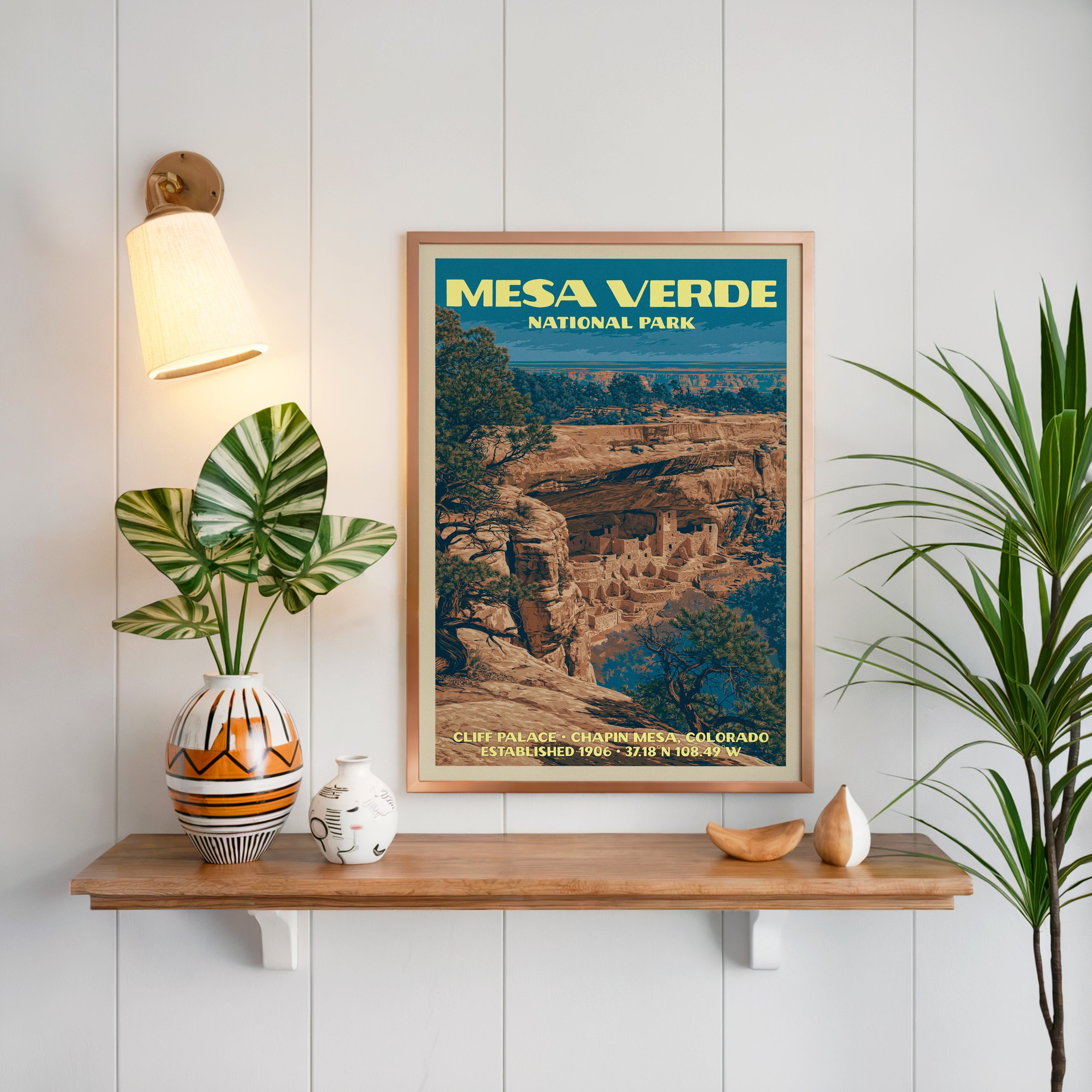 Cliff Palace Mesa Verde print framed on white panelling above an oak shelf with a patterned vase and brass sconce
