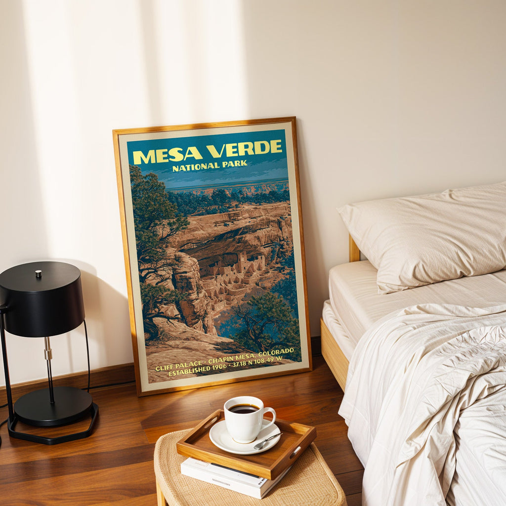 Cliff Palace Mesa Verde poster in a gold frame on the floor beside a made bed and a black table lamp
