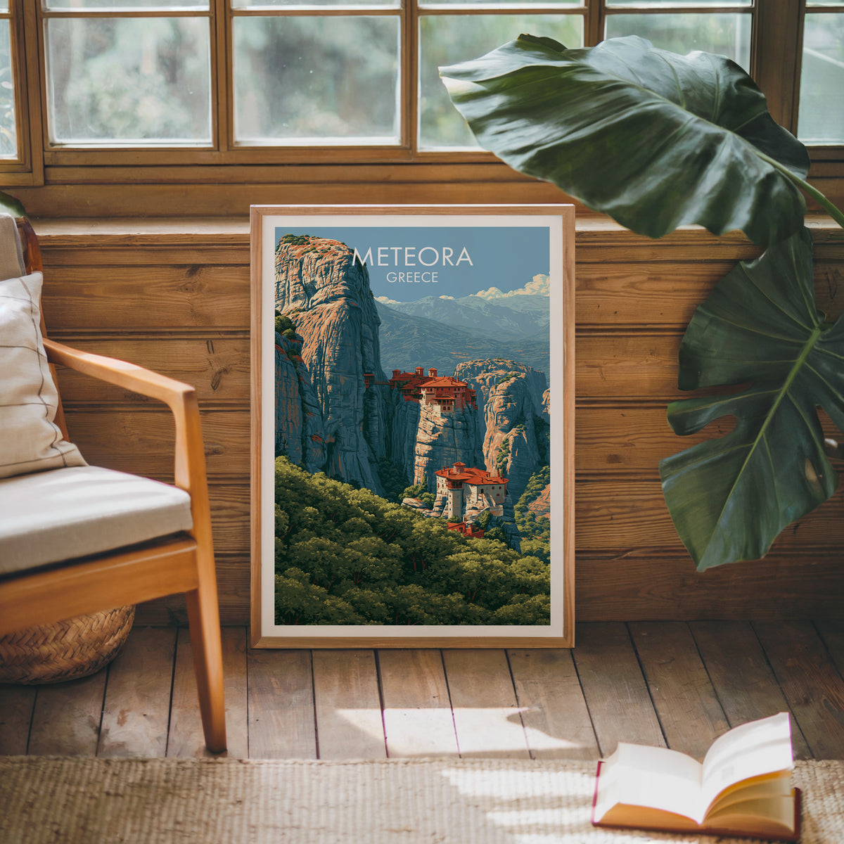 Meteora travel poster, oak frame leaning on a wood-panelled sunroom wall by a mid-century armchair