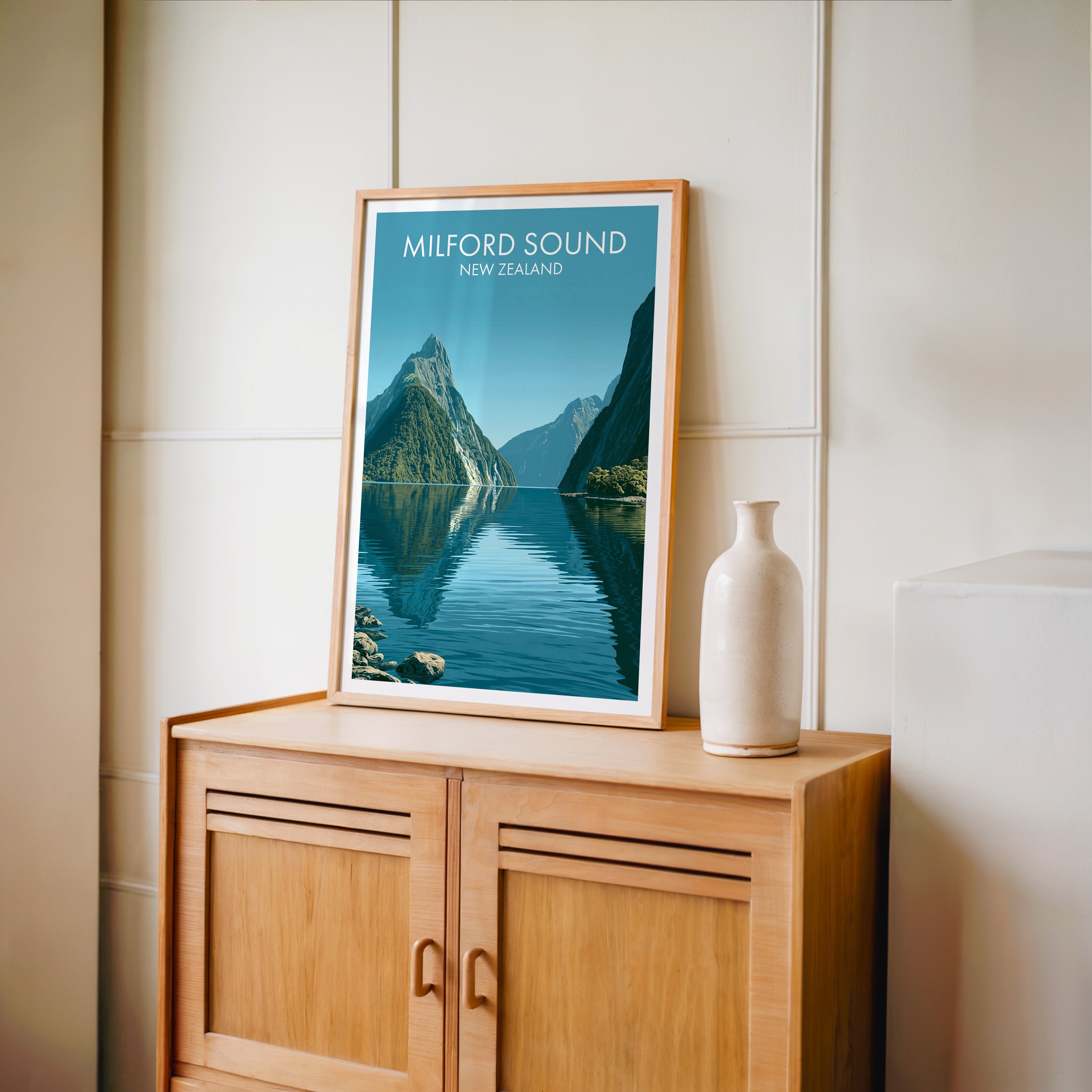 Fiordland travel poster in an oak frame on a light oak cabinet beside a tall pale bottle vase