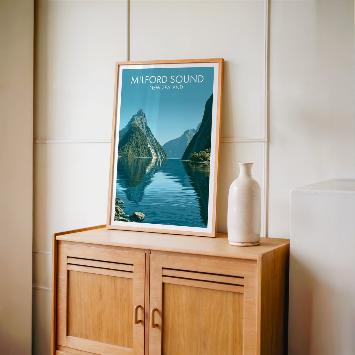 Fiordland travel poster in an oak frame on a light oak cabinet beside a tall pale bottle vase