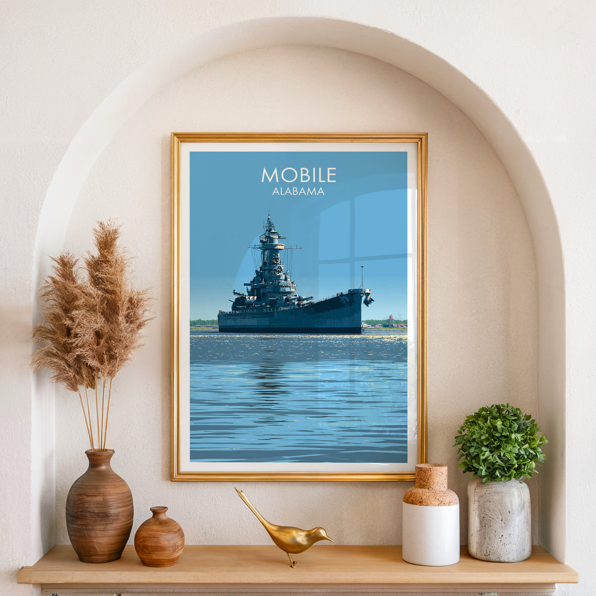 Alabama battleship canvas print in a gold frame inside an arched wall niche with pampas grass and a brass bird