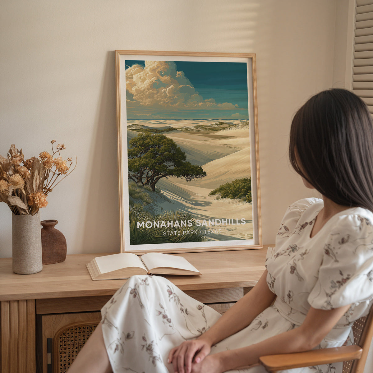 A woman in white sits beside the oak-framed Monahans Sandhills print on a wood sideboard