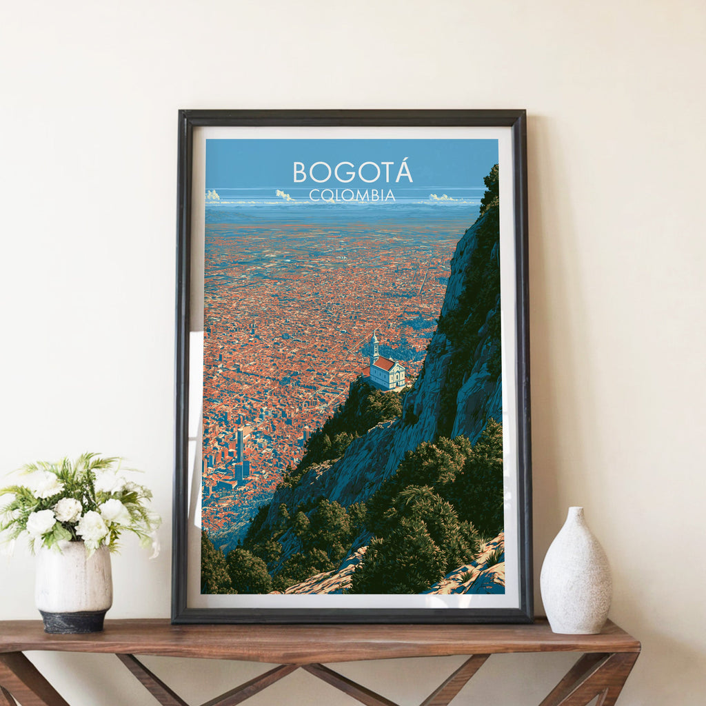 Bogota hilltop church poster in a black frame on a brown X-leg console with white blooms and a ceramic vase