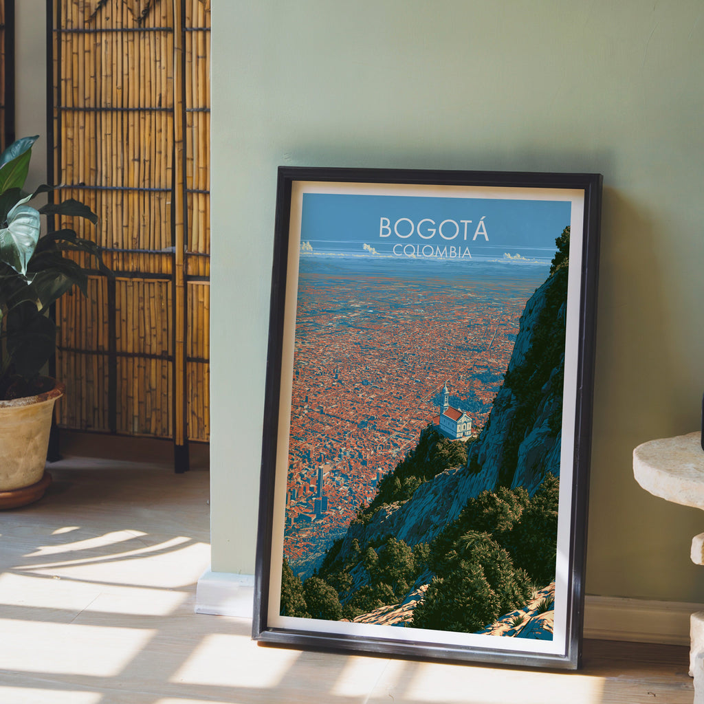Bogota cityscape art in a dark brown frame on pale wood flooring by a sage green wall, bamboo screen and clay pot