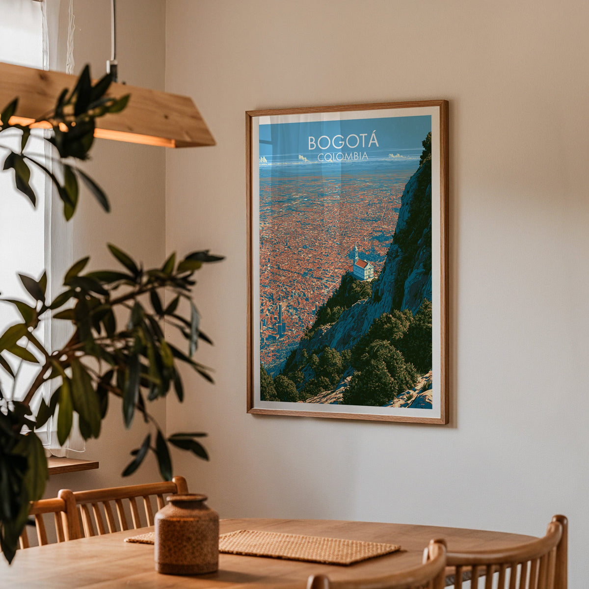 Terracotta city view art in an oak frame in a dining corner with a wood table, cane chairs and an olive branch