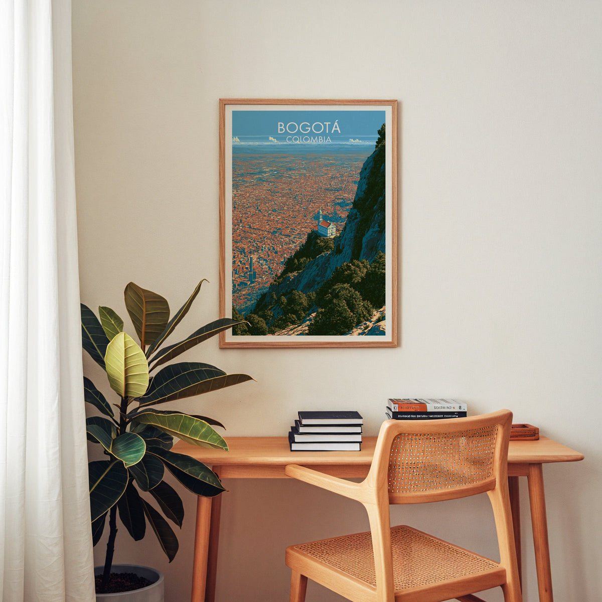 Colombia travel poster in an oak frame above a wood desk with a cane chair, books and a rubber plant in a home office